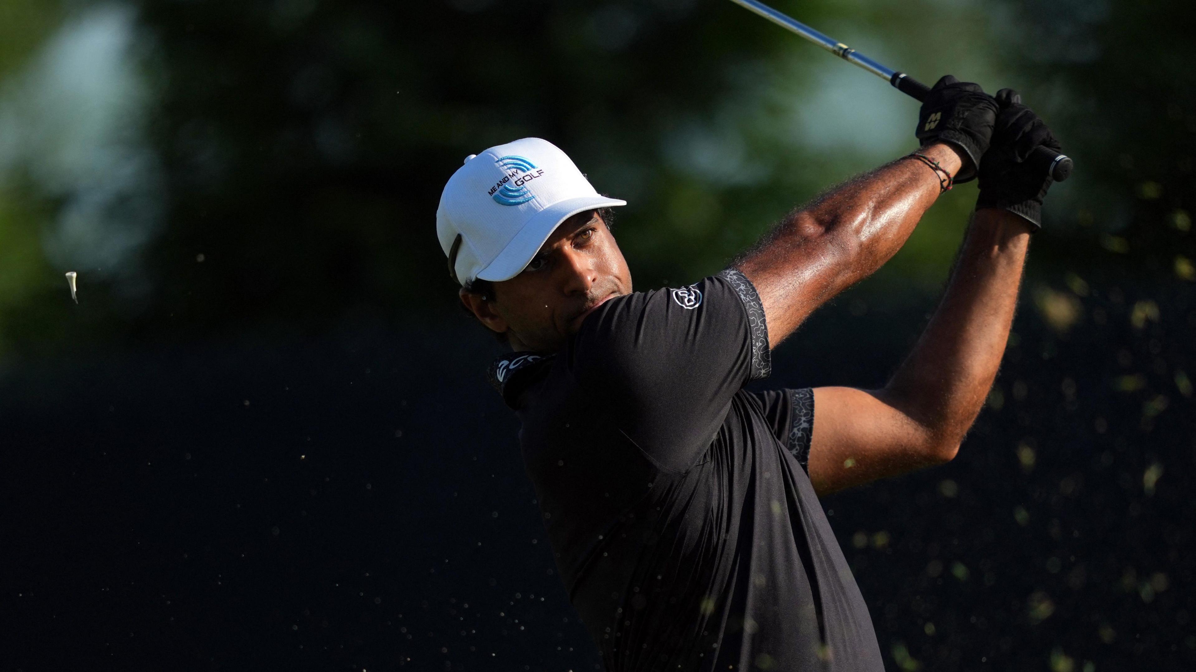 Aaron Rai mid swing wearing a black t-shirt and white cap
