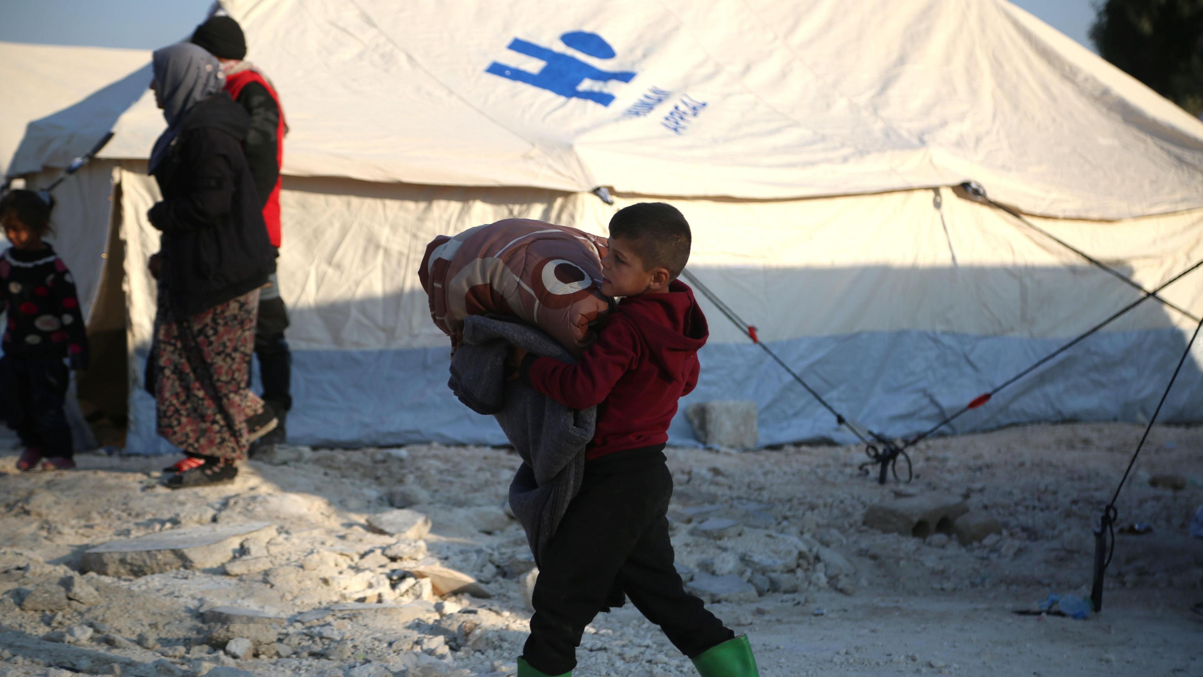 A boy carries a blanket at a camp for displaced people in al-Bardaqli, near the city of Sarmada, north of Idlib, Syria (28 November 2024)