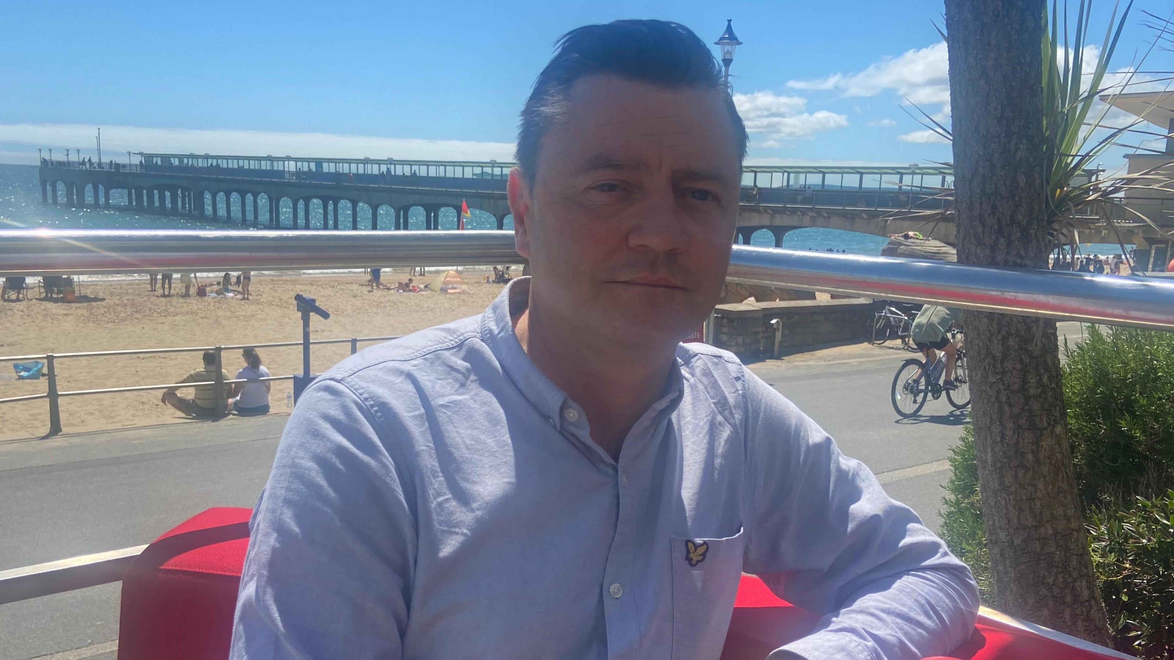 Lib Dem John Martin Nicholas wears a blue shirt while sitting on a red sofa