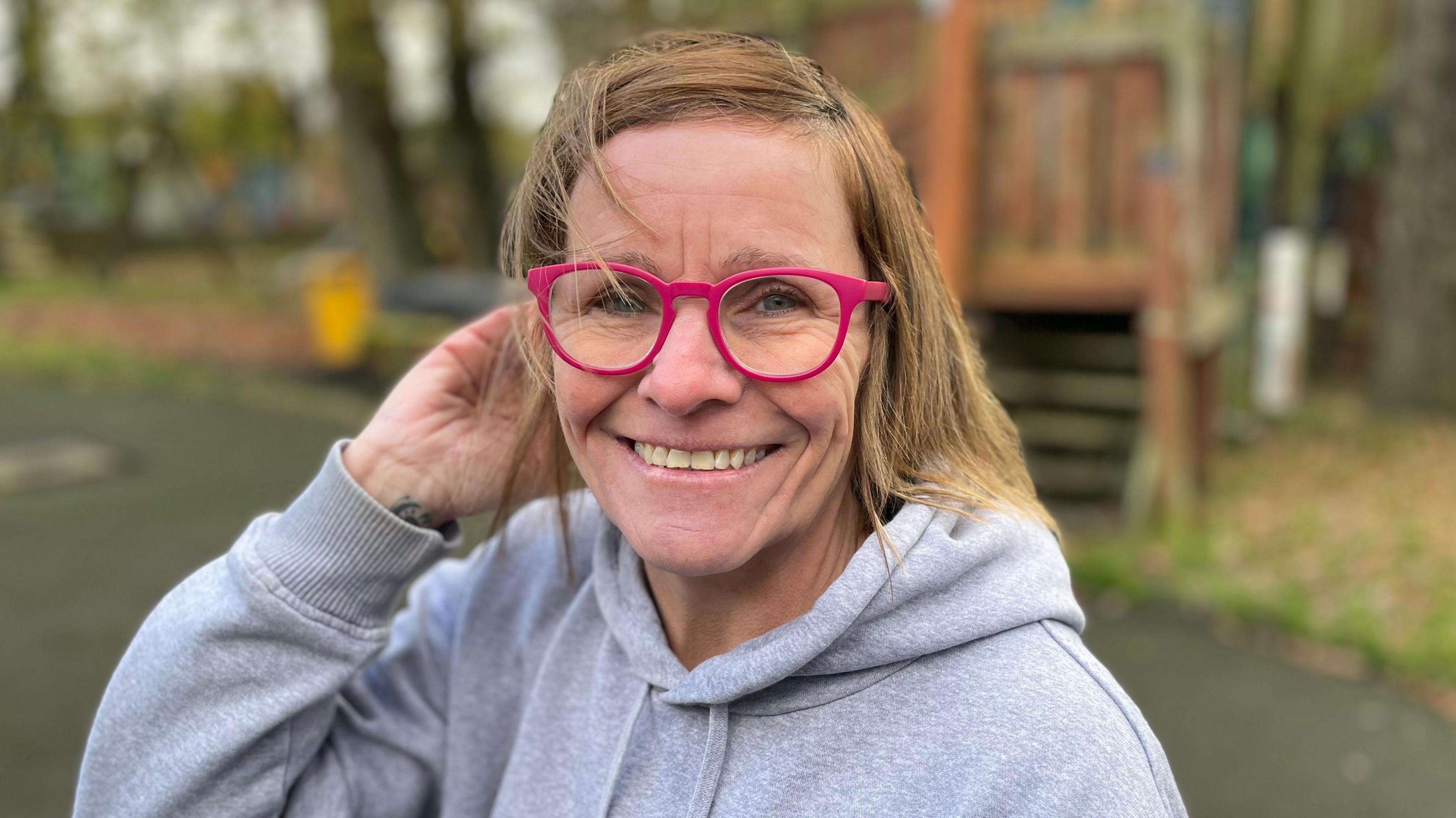 A woman wearing glasses and a hoodie, smiling at the camera