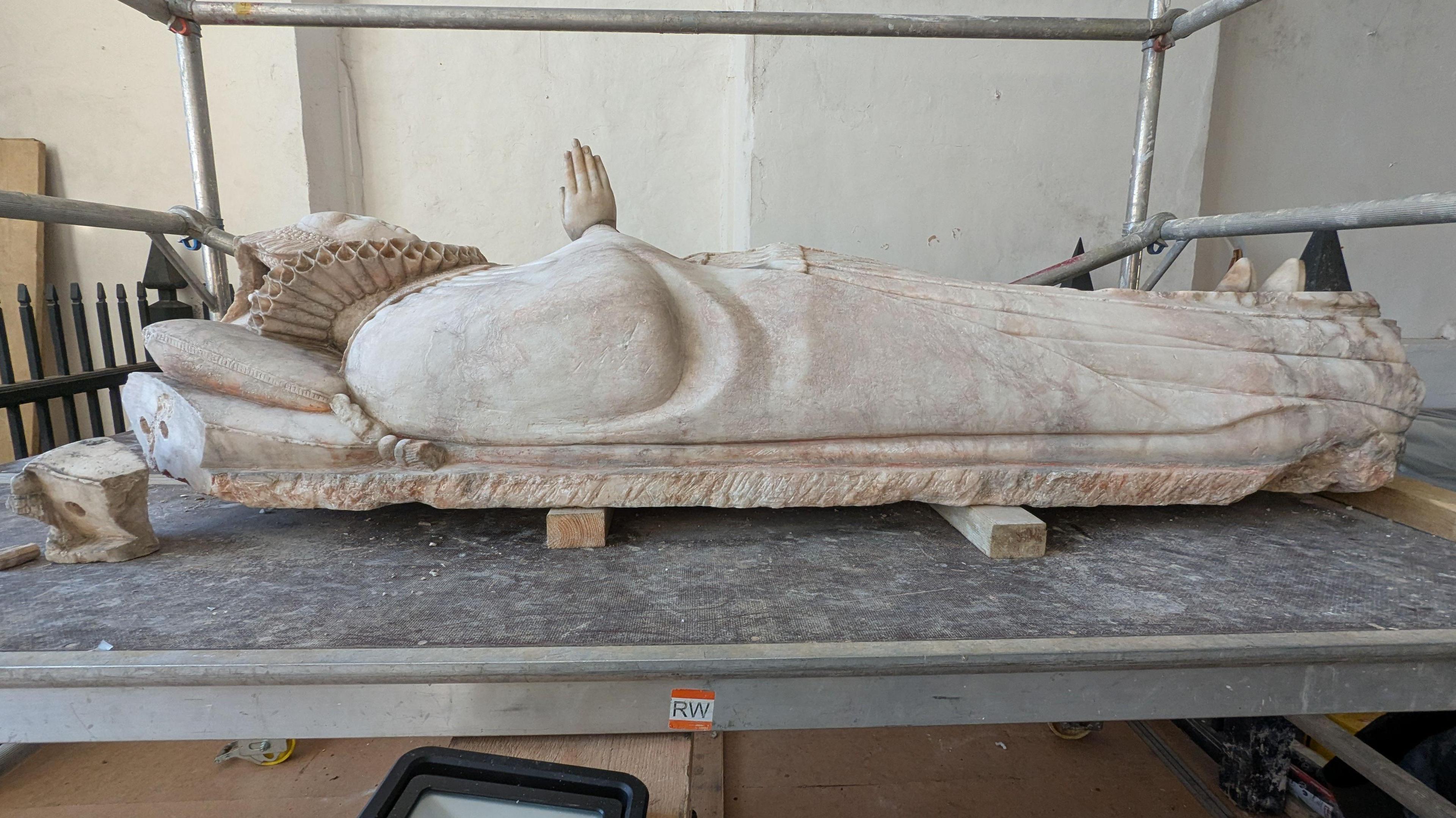 A statue of a woman in a robe lying on her back with her palms together 