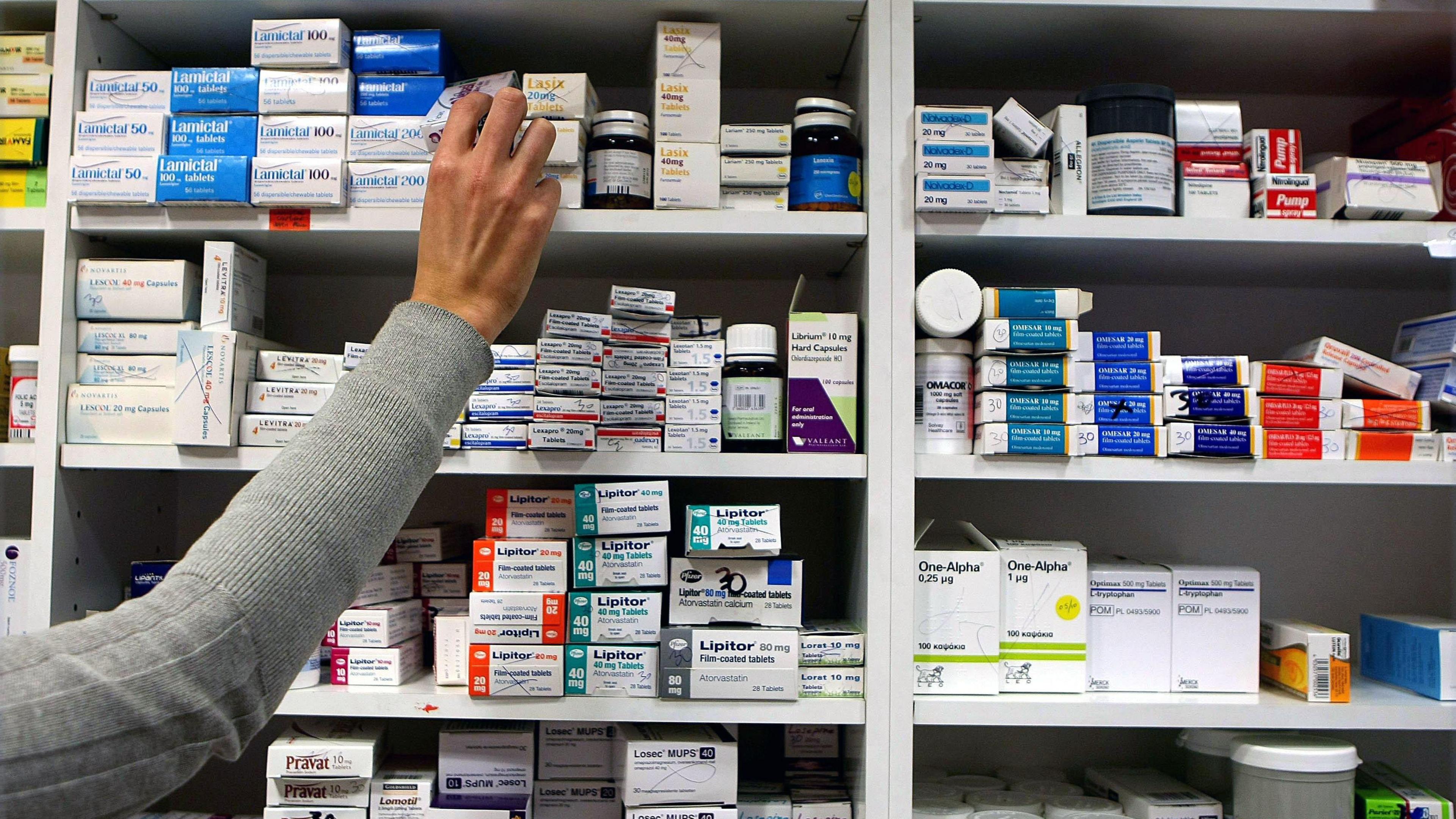 Wall with shelves full of medicine boxes, with an arm extended to top shelf picking up one of the boxes.