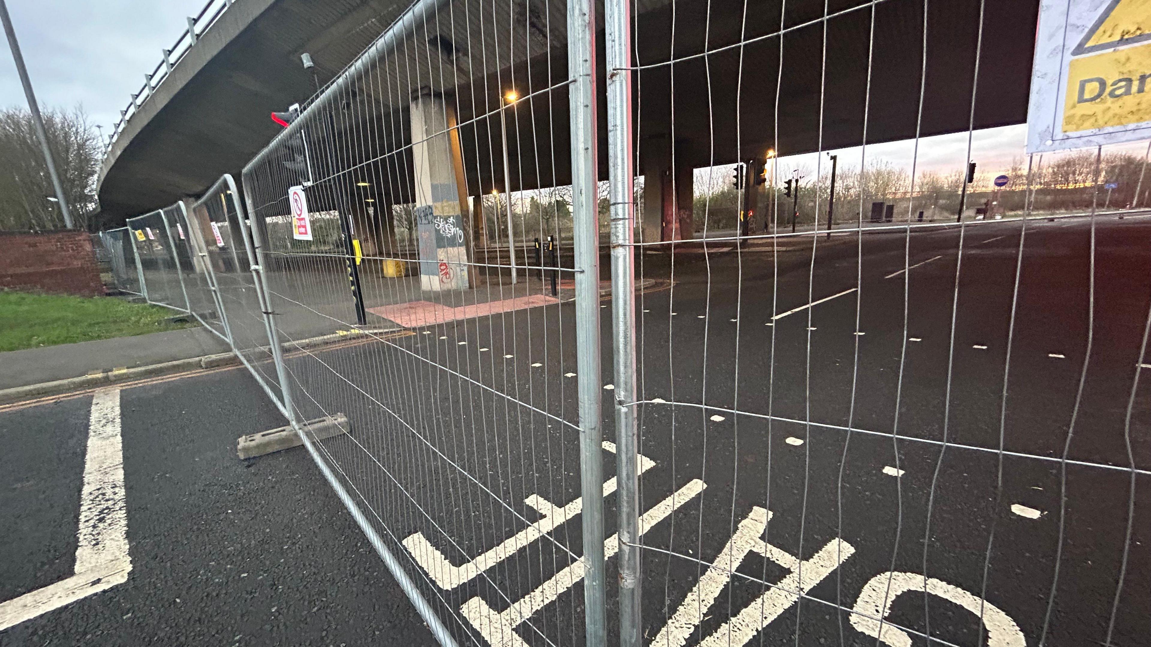 Metal fences blocking off the road underneath the flyover and a pedestrian crossing.