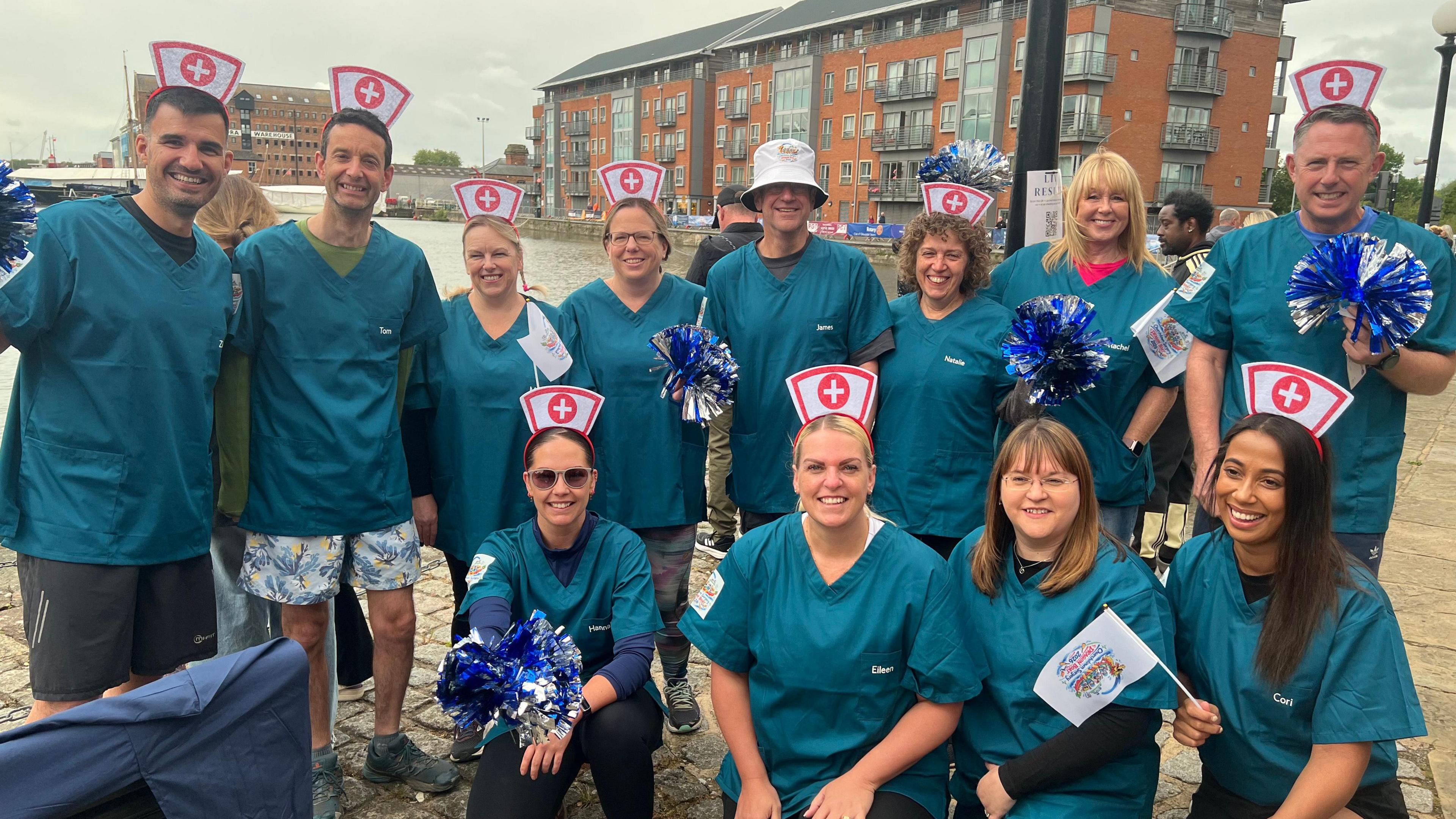 Two rows of people in nurses outfits are standing and kneeling, looking at the camera and smiling.