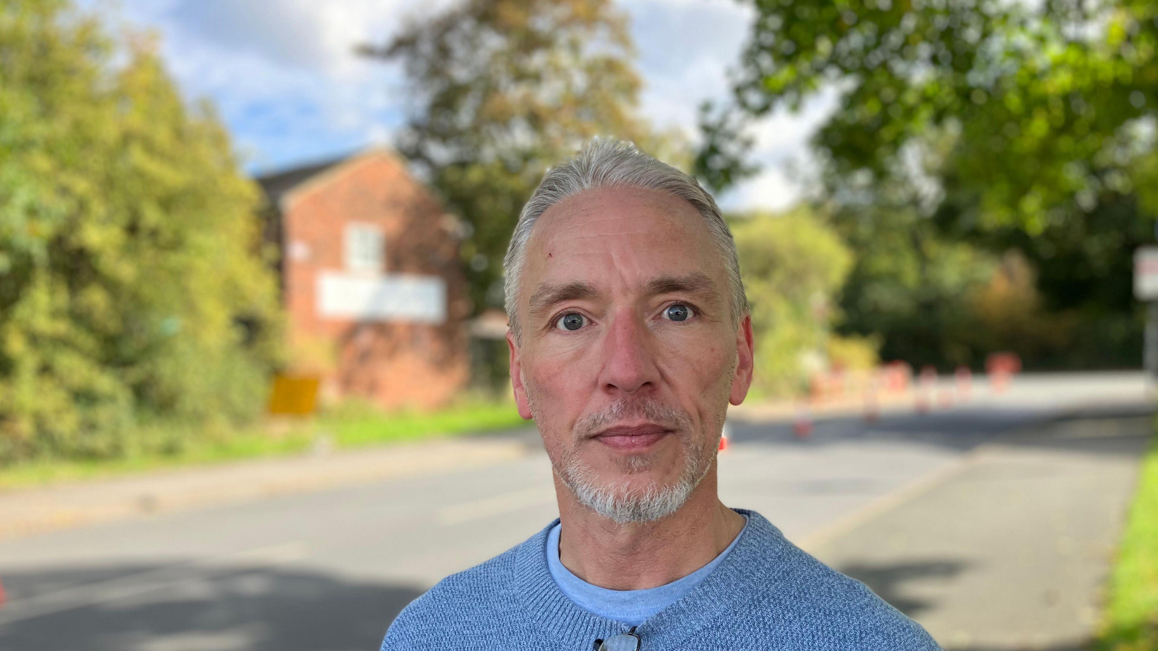 A man with short grey hair wearing a blue jumper