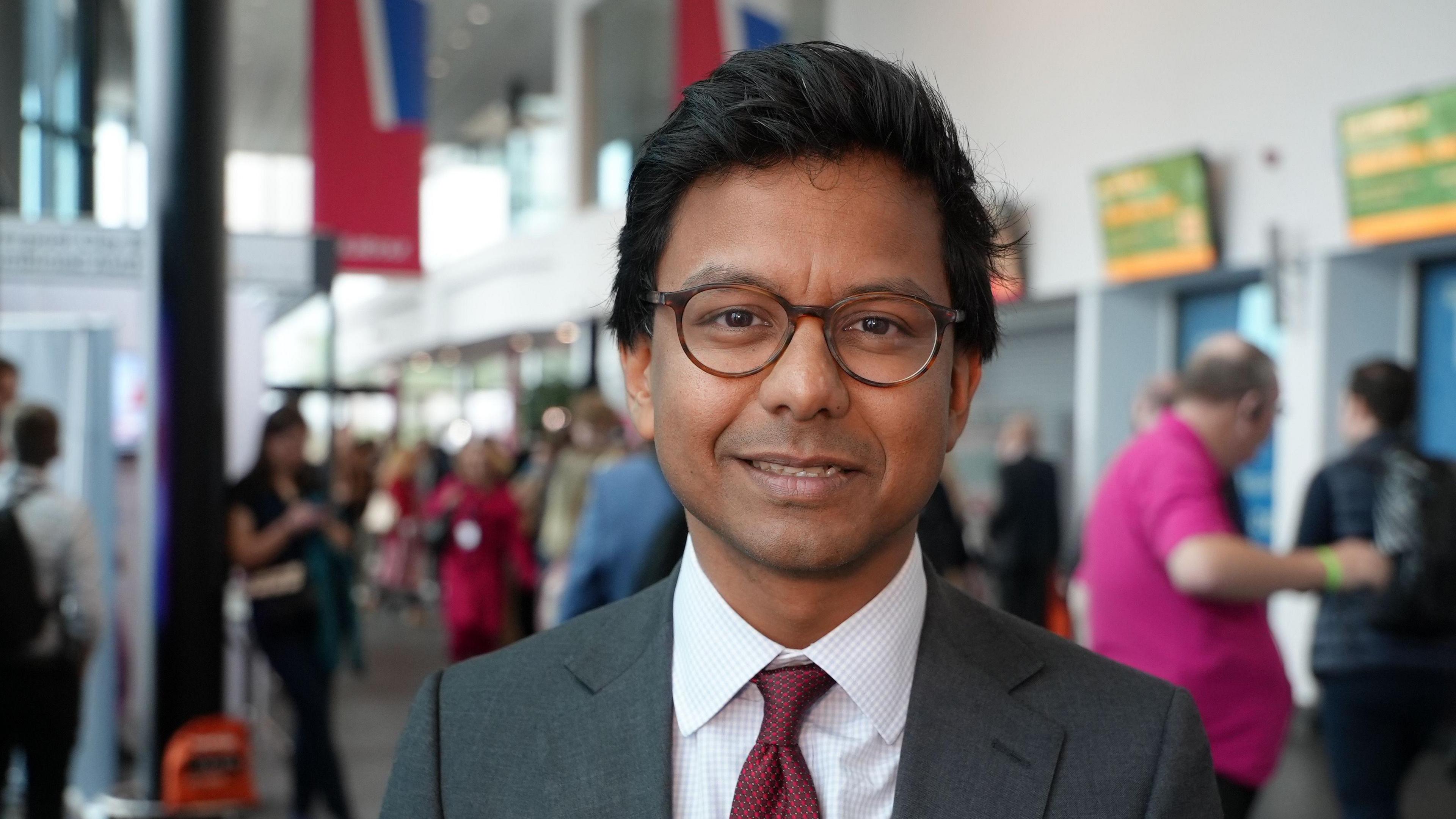 Kanishka Narayan smiles as he looks at the camera. The background is blurred but he appears to be at a conference or event.