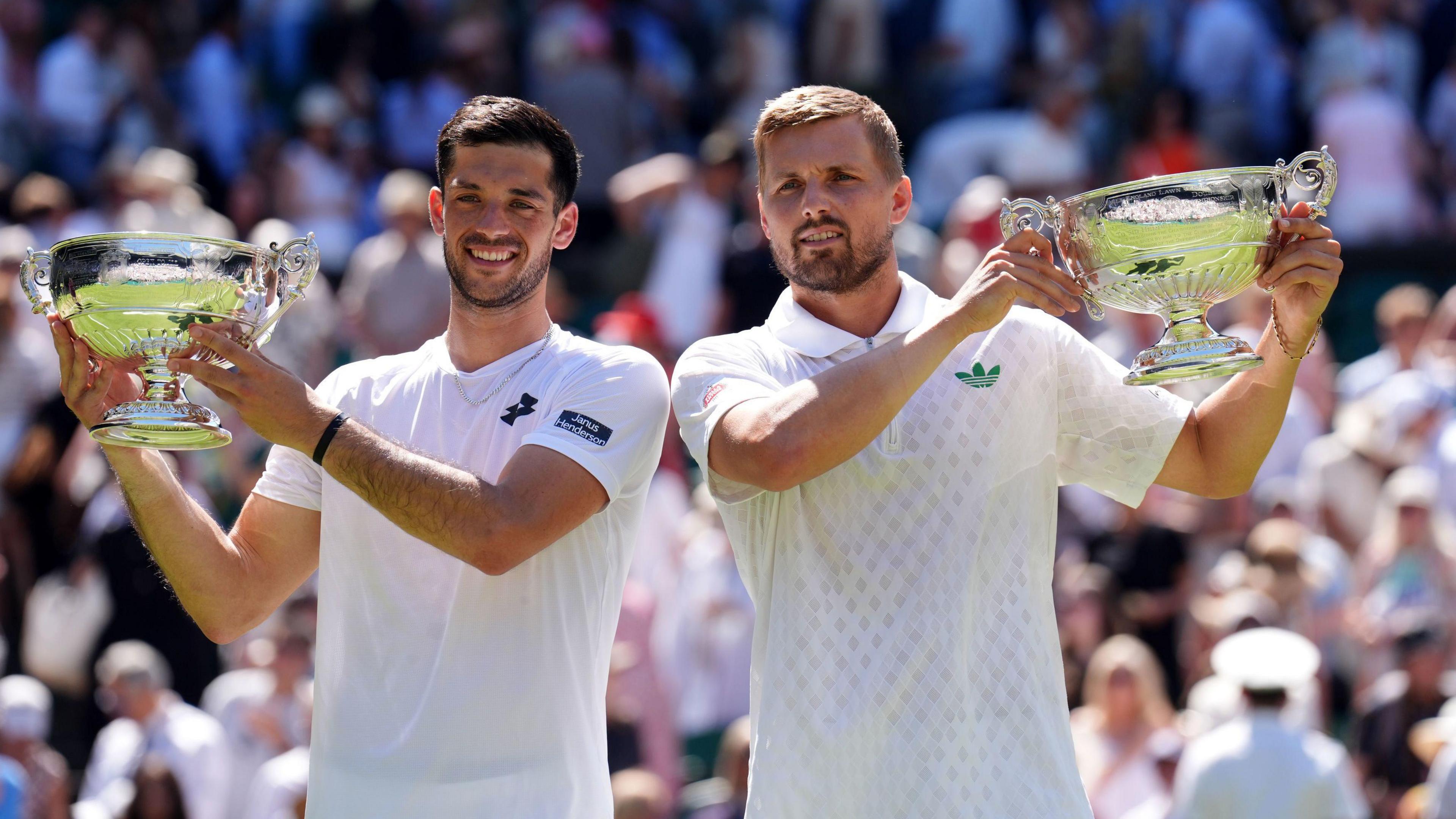 Julian Cash (L) and Lloyd Glasspool (R) smile as they hold up their Wimbledon trophies.