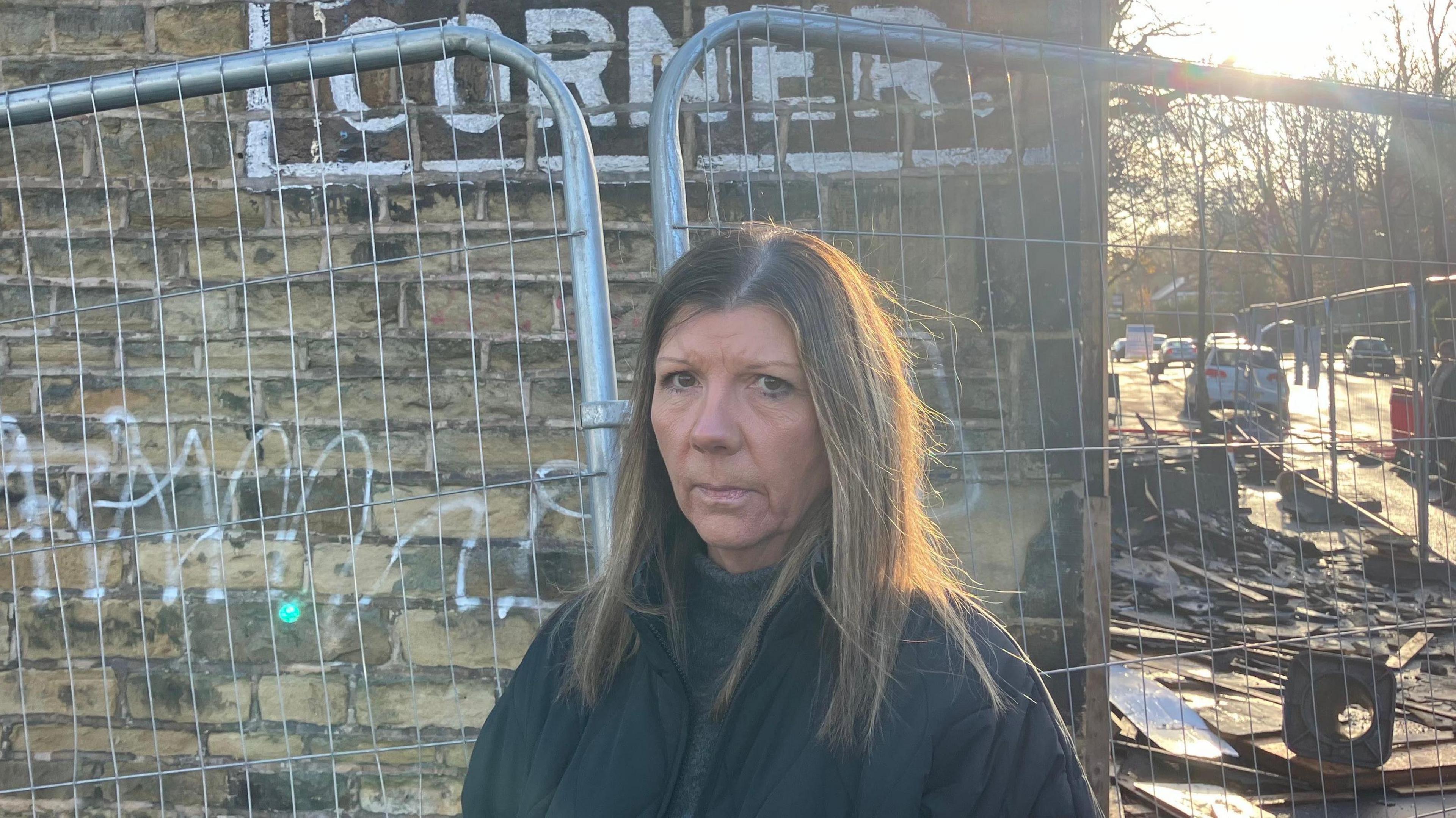 Kelly Hildreth stood next to fences surrounding her business. She wears a dark jacket and a neutral expression.