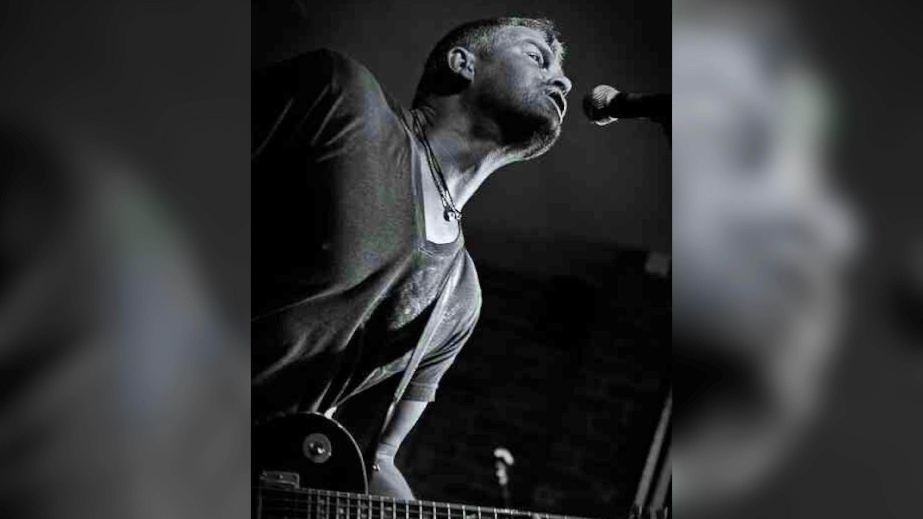 A black and white image of John Brindle performing with a guitar, while singing into a microphone.