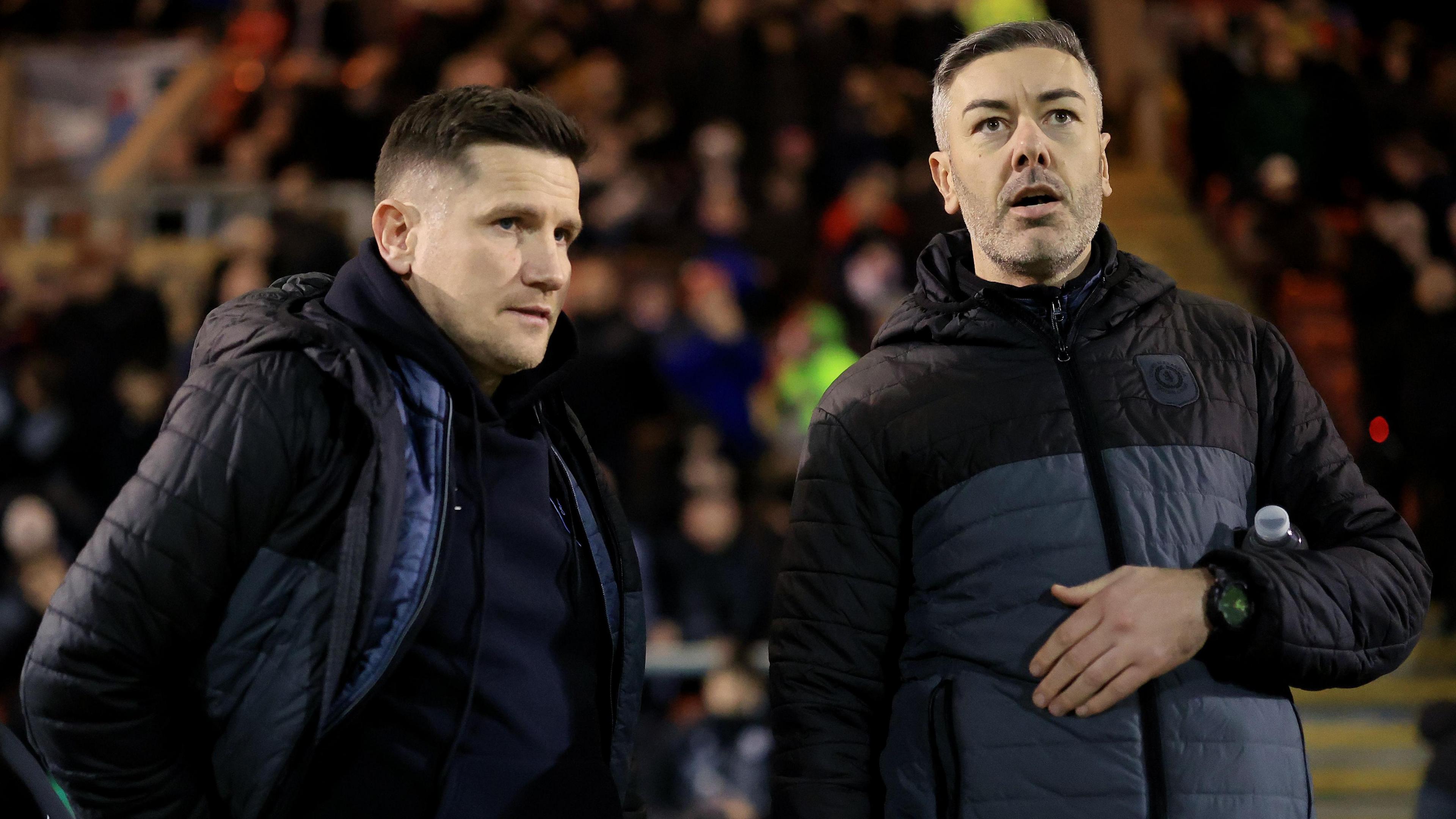 Ryan Dicker on the right of the picture talks to Crewe manager Lee Bell on the touchline during a match