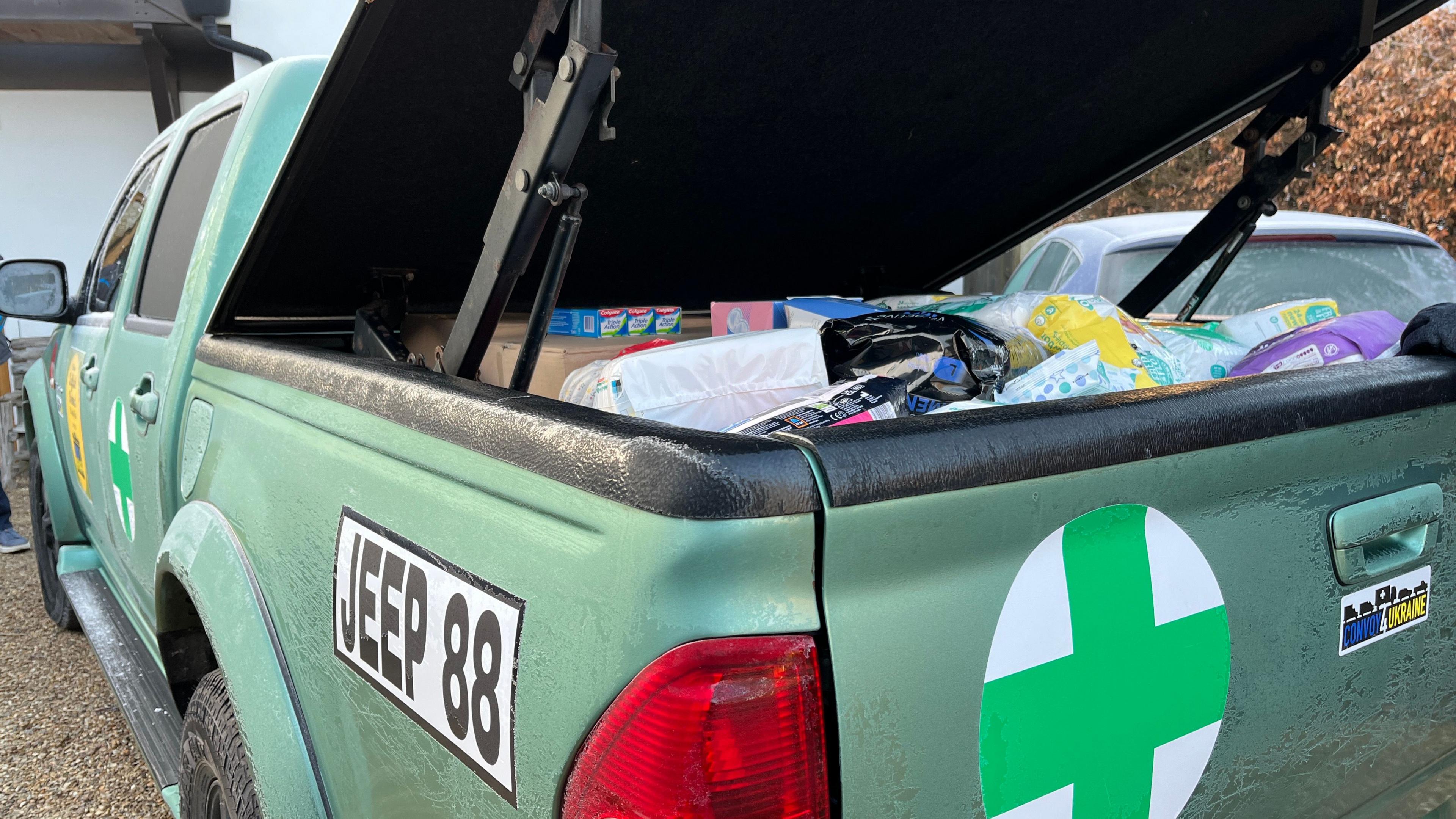 The back of the humanitarian aid 4x4 car. Inside the boot, which is open, are medical supplies. There are medical stickers on the outside of the car. 