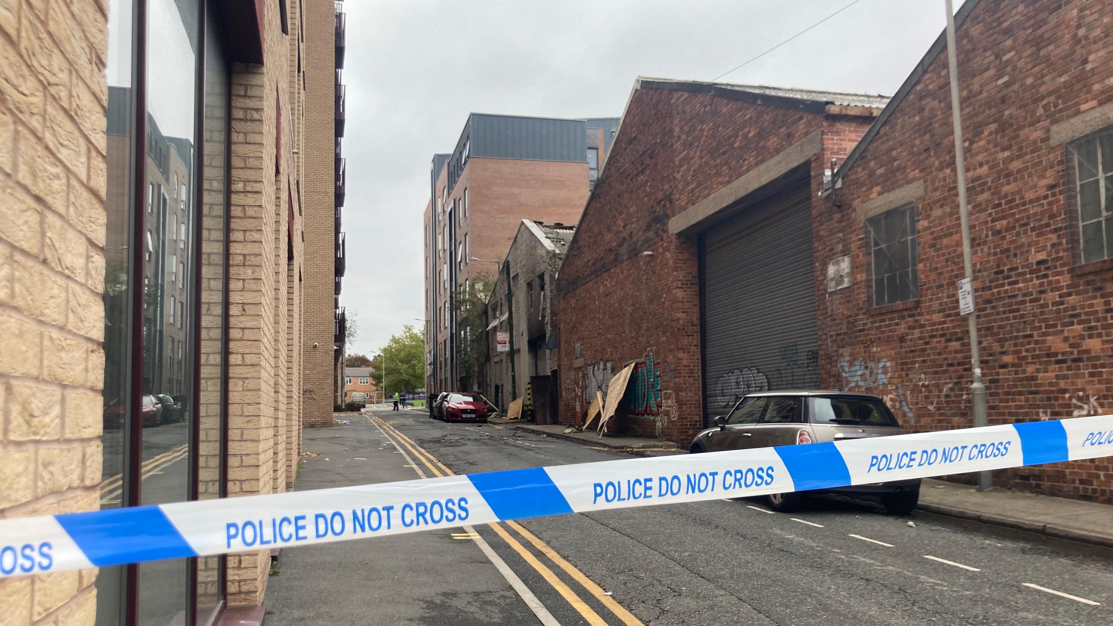 Police tape says 'Police do not cross' with the fire damaged warehouse building behind.