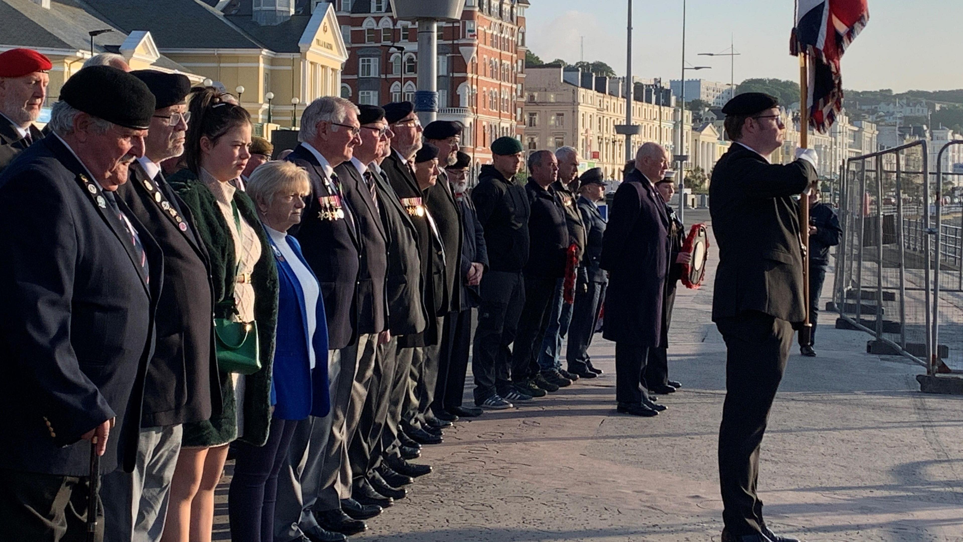 Men and women wearing medals standing to attention behind a flag bearer