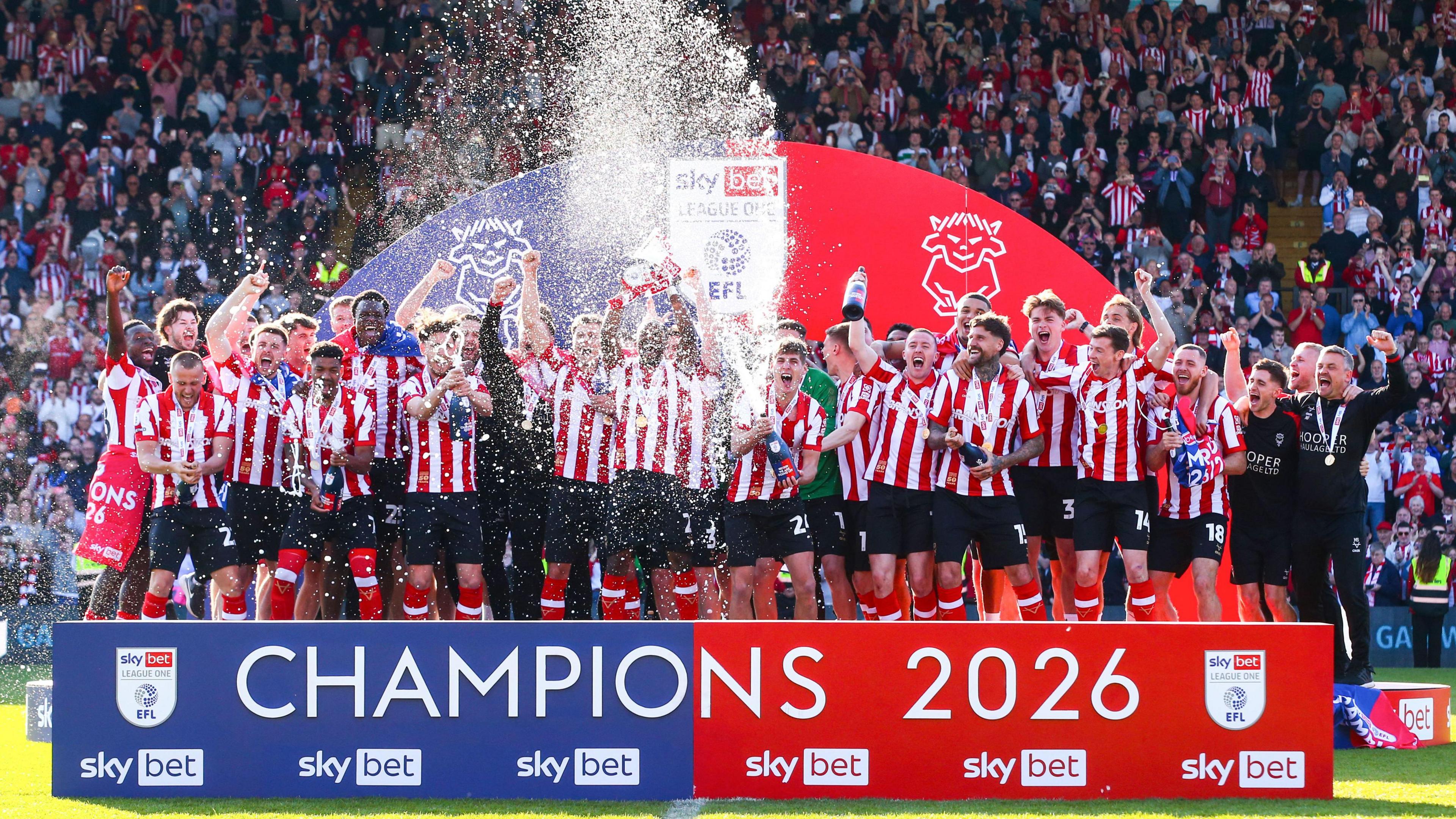 Lincoln City's players in their playing kit lift the League One championship trophy