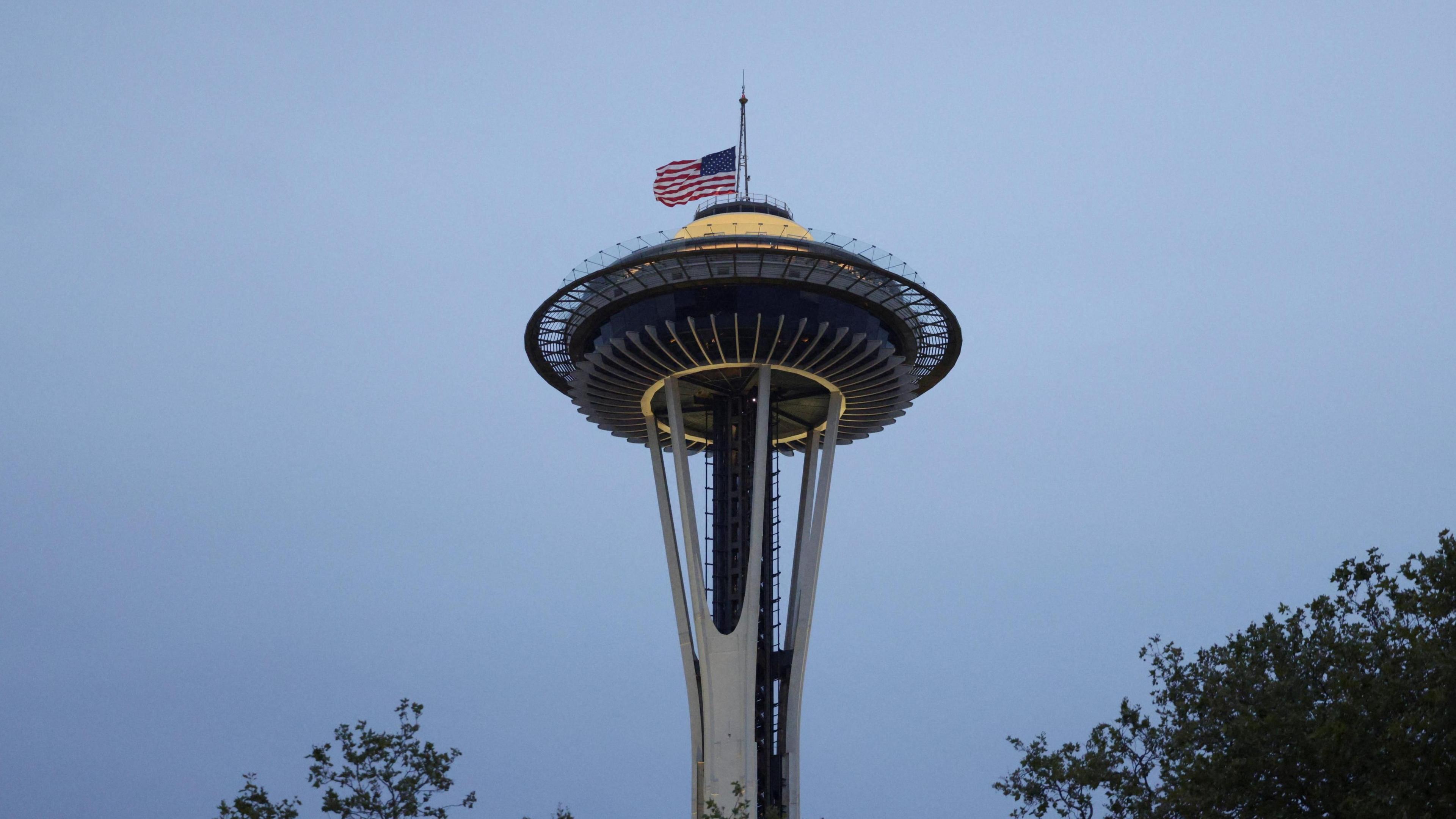 The Seattle Space Needle building on a twilight background. A large US flag is flying at half-mast as a tribute to the shooting victims.
