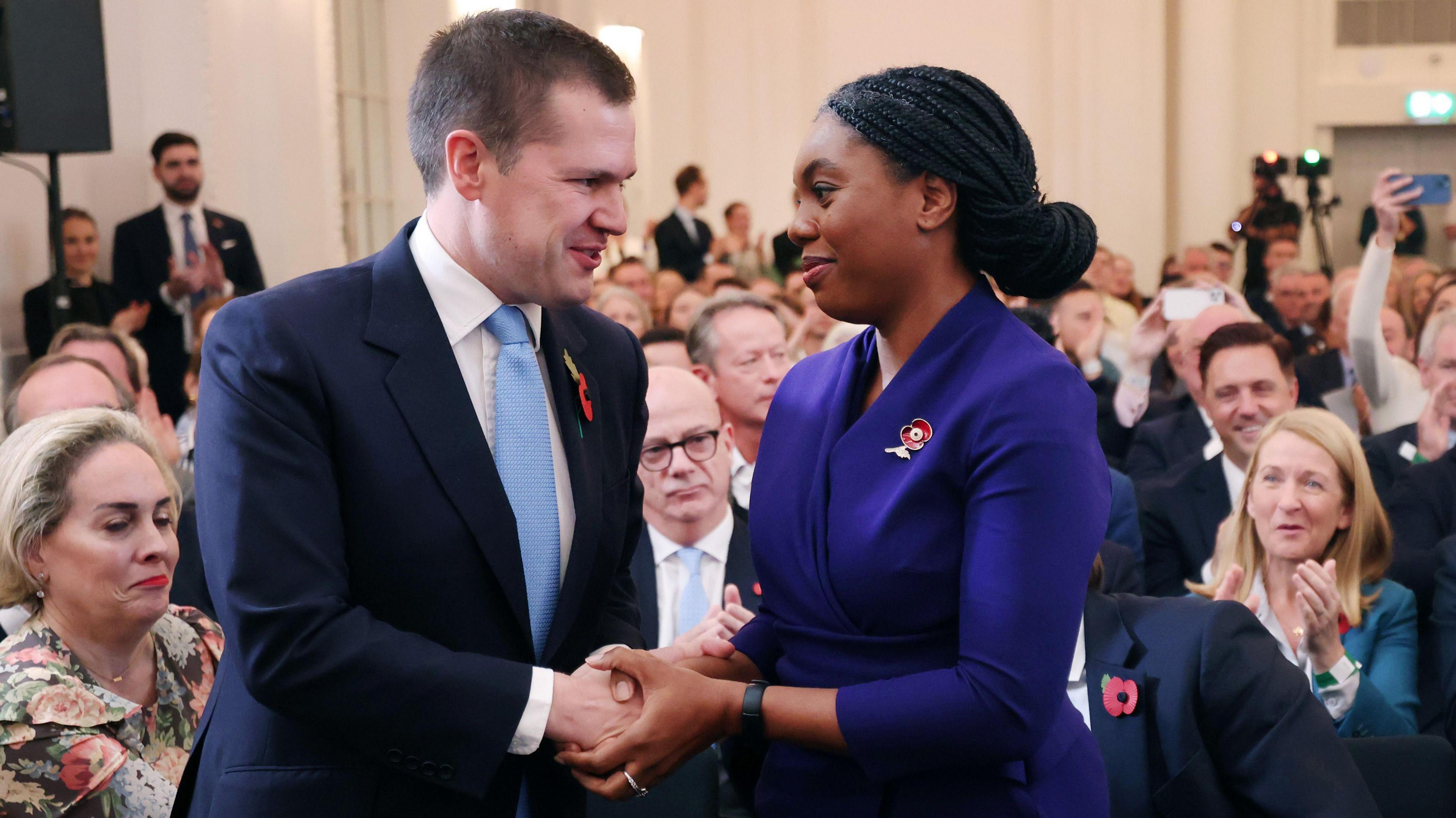 Robert Jenrick and Kemi Badenoch shake hands in front of a clapping audience, after she is announced as the new Conservative leader