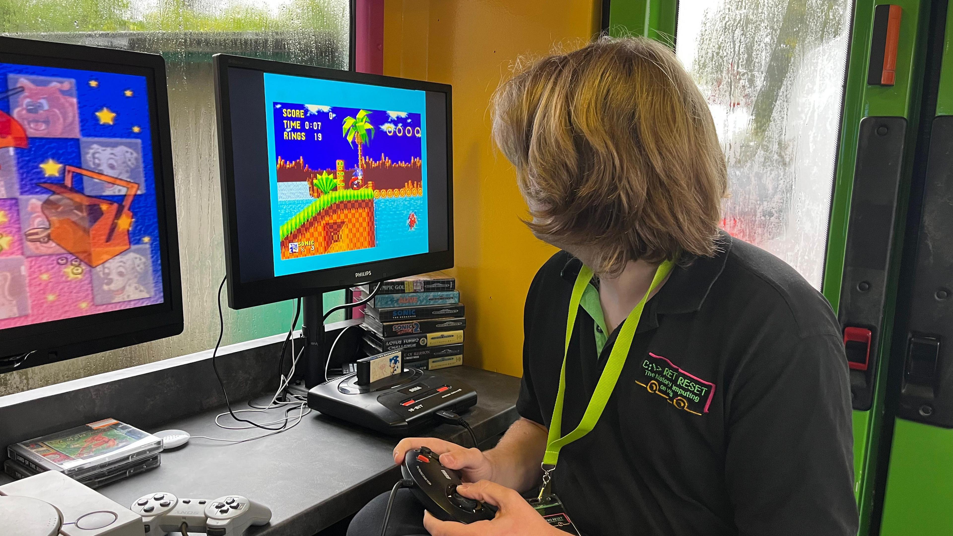 Luke playing sonic the hedgehog on a sega dreamcast sat in the bus holding a remote