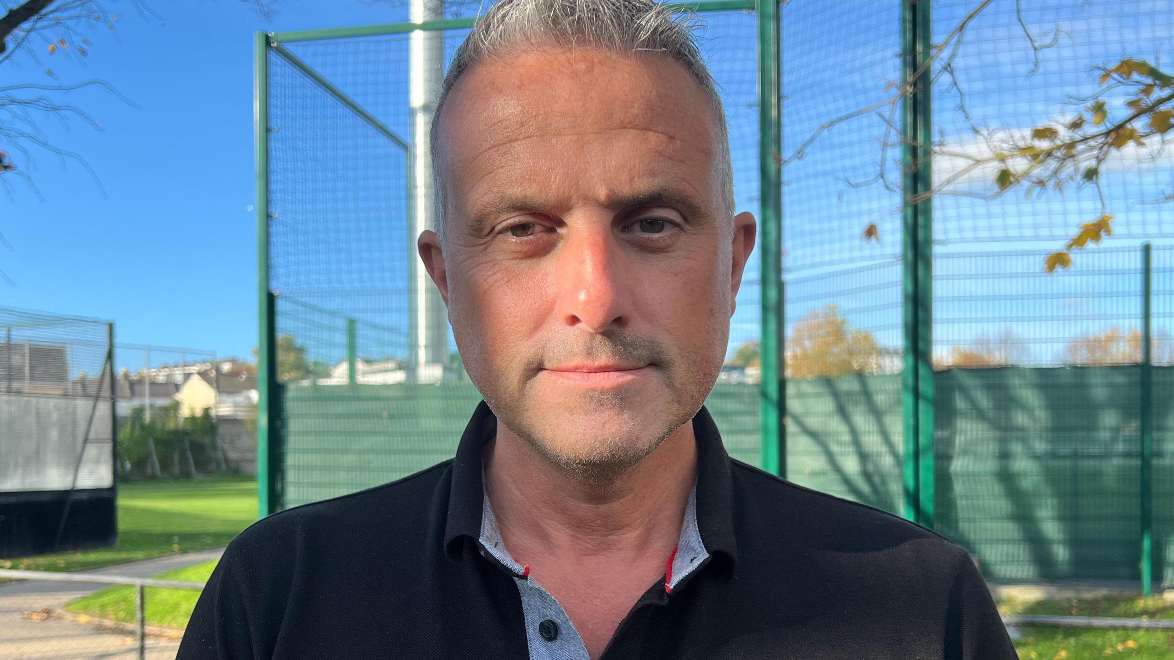 Carl Walker is looking into the camera. He has short grey hair and is wearing a black polo shirt.