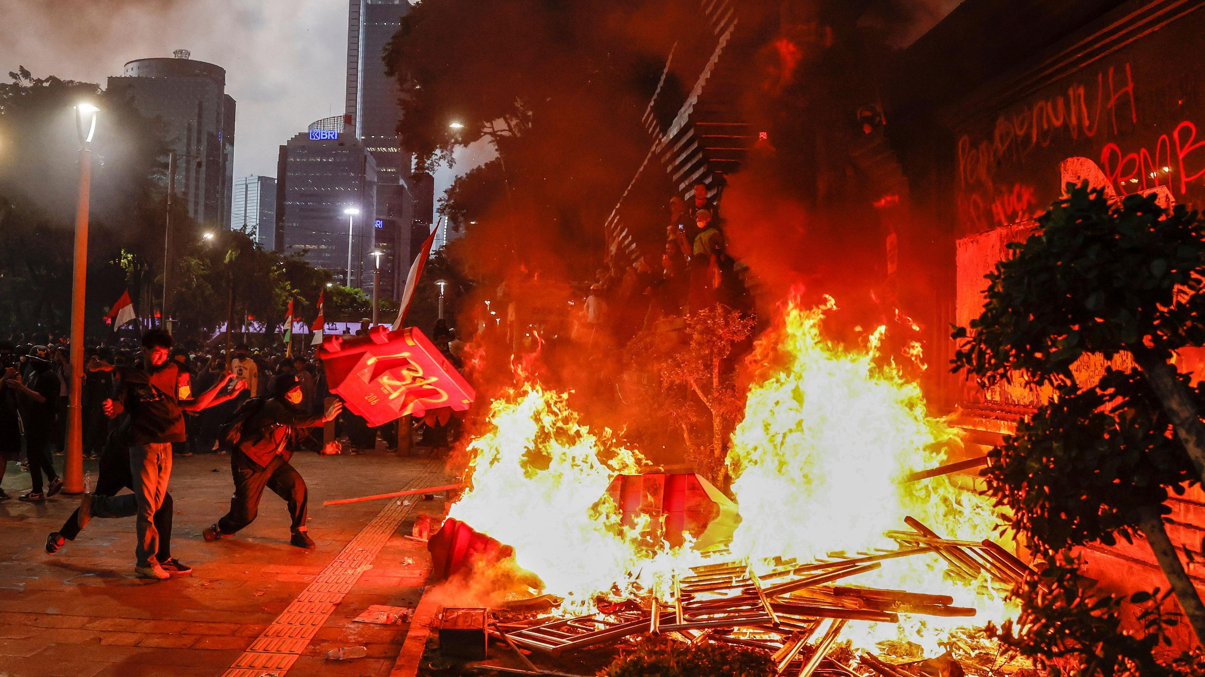 Protesters are seen placing road barriers onto a fire outside a police headquarters in Jakarta
