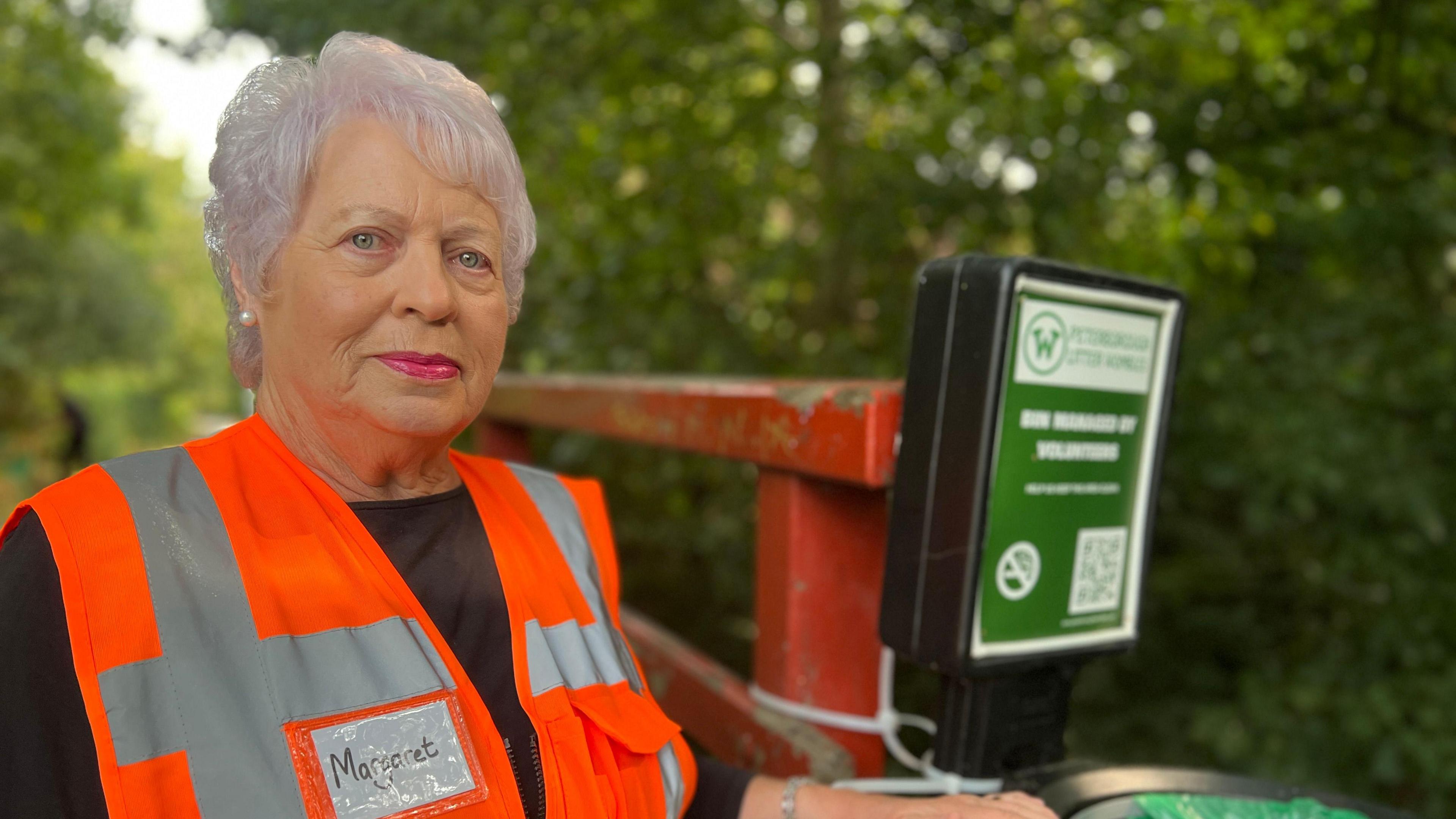 Woman in high visibility jacket next to a rubbish bin sign