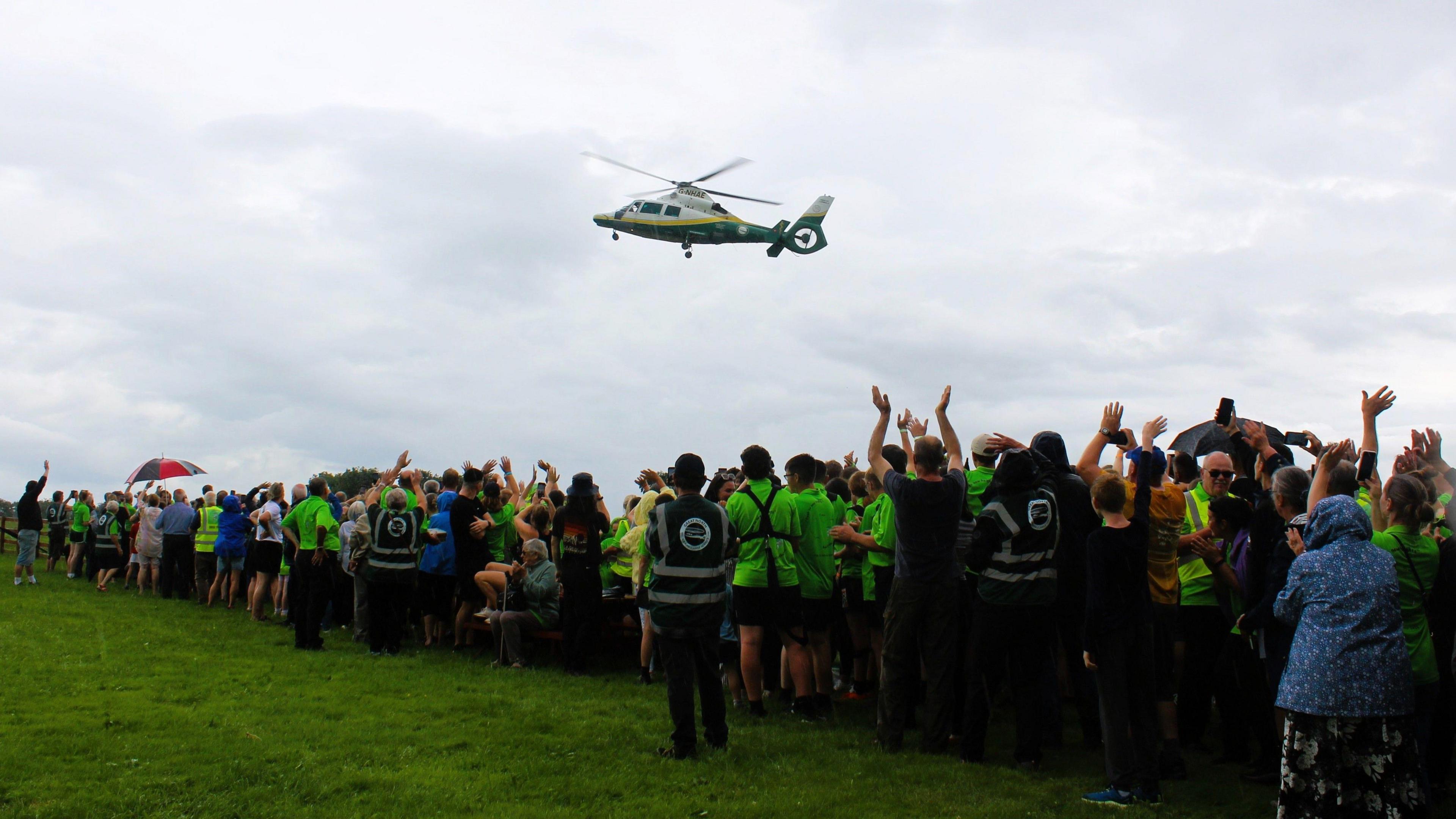 Dozens of people, most of them wearing the bright green t-shirts, are waving at the Great North Air Ambulance helicopter in flight overhead. Some are clapping.