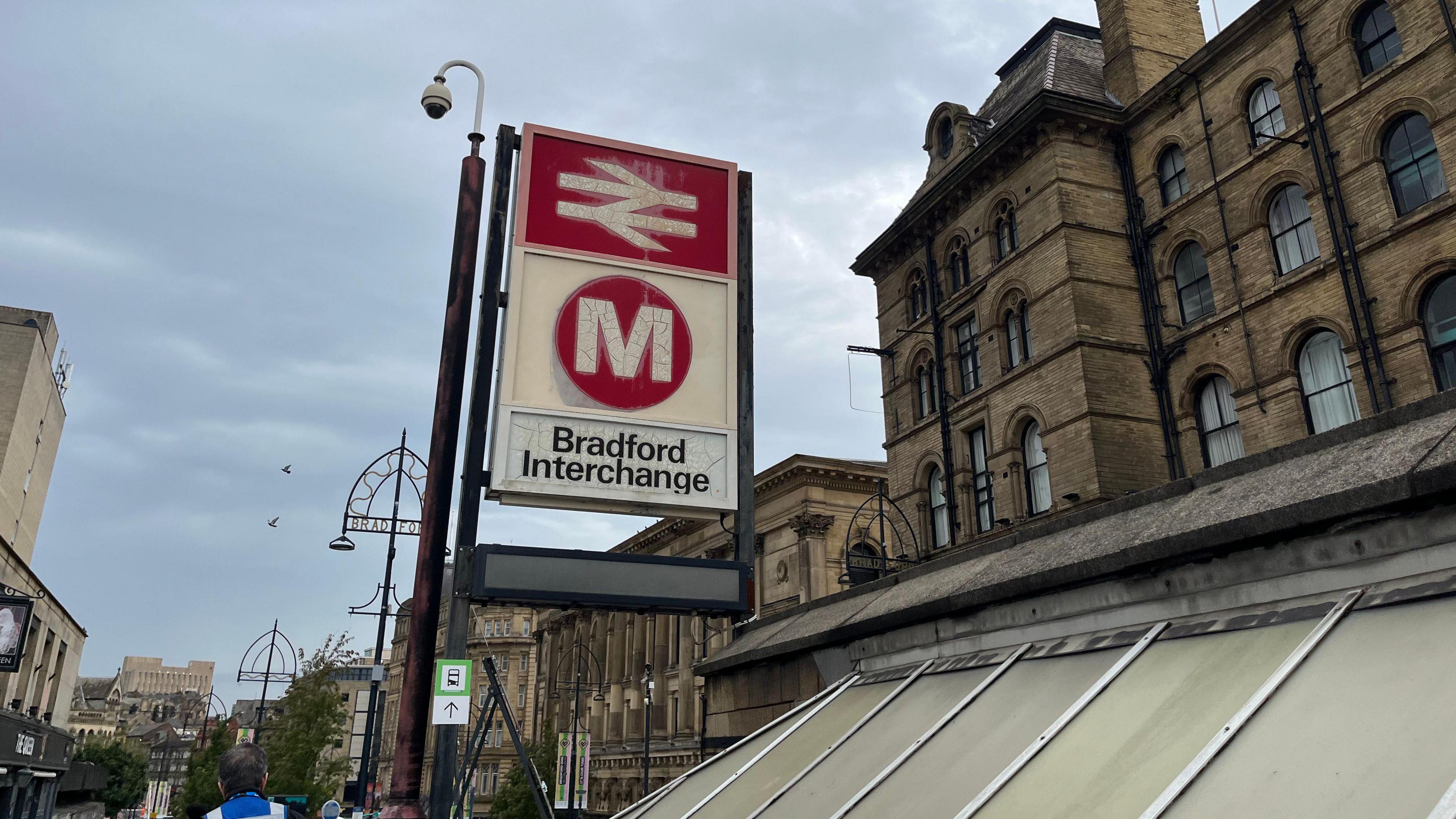 Bradford Interchange, with a view looking up to a sign indicating it is both a bus and a rail station. In the distance is St George's Hall and other city centre buildings. 