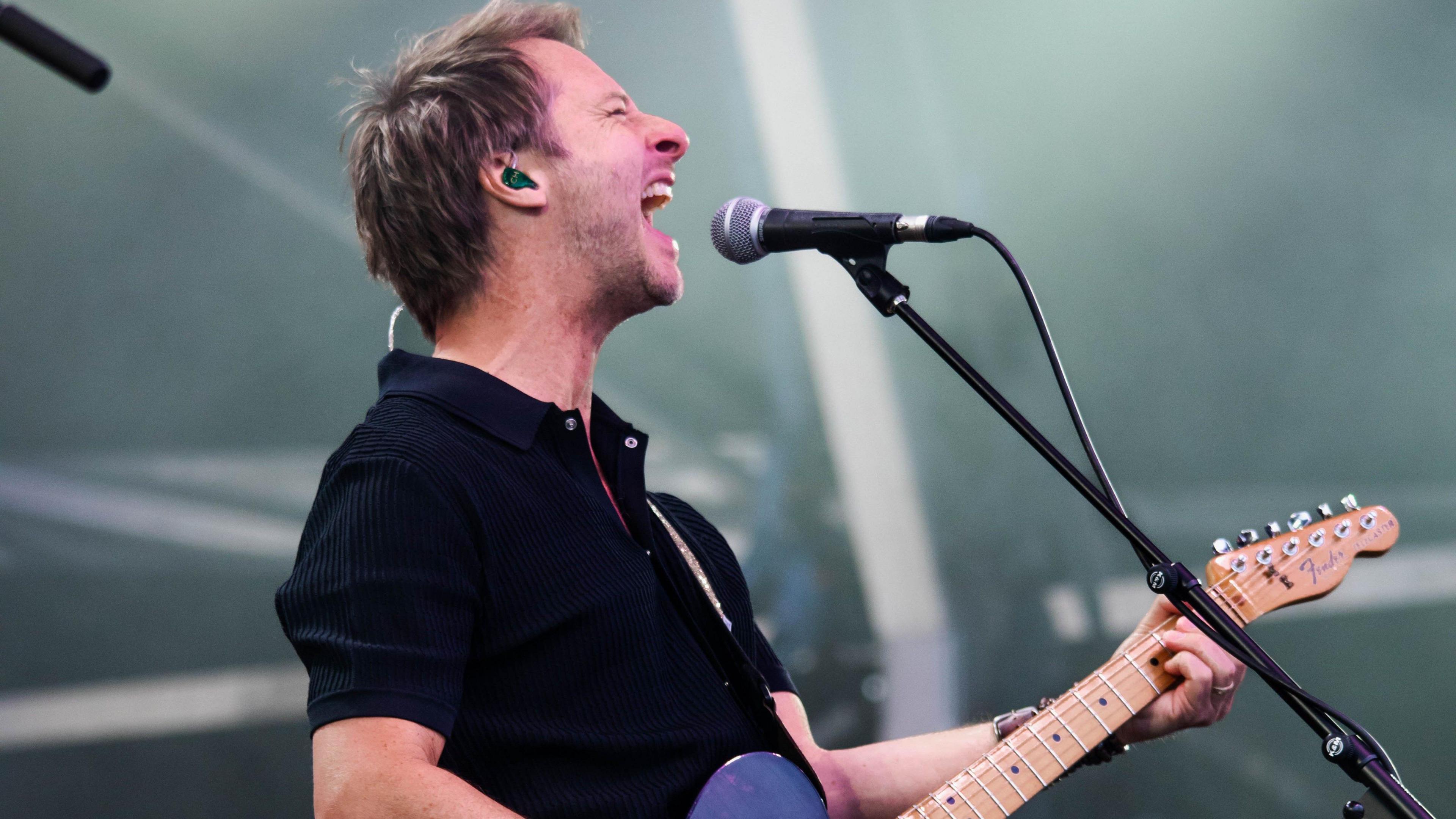 Chesney Hawkes sings into a microphone while playing an electric guitar at the Good Times Live event in Bristokl