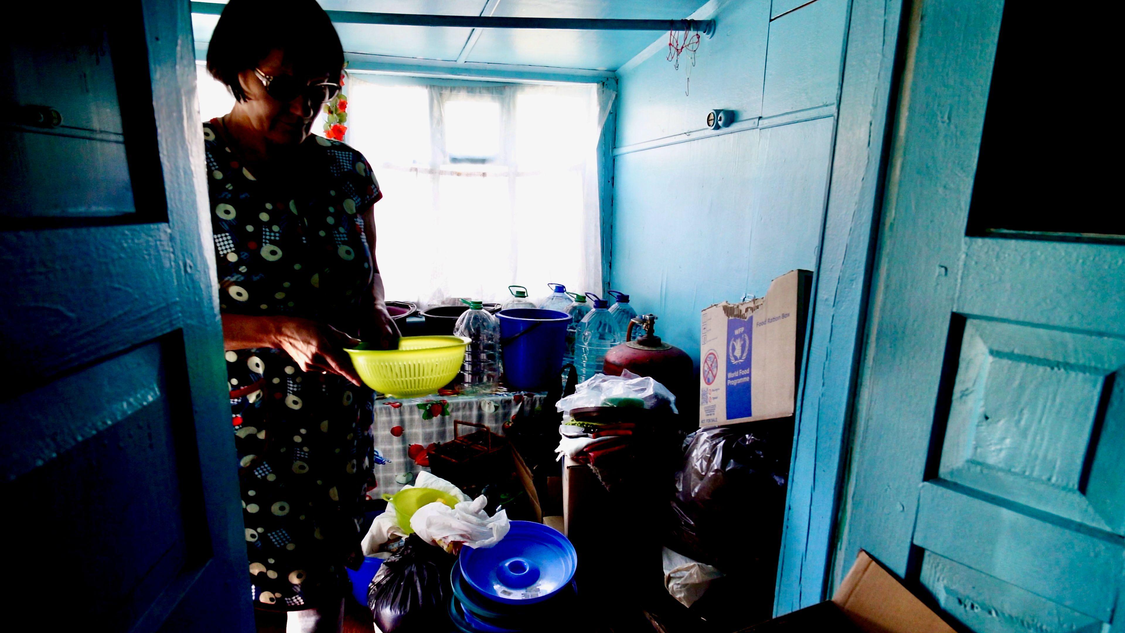 Olha stands in her home, filled with bottled water and rubbish