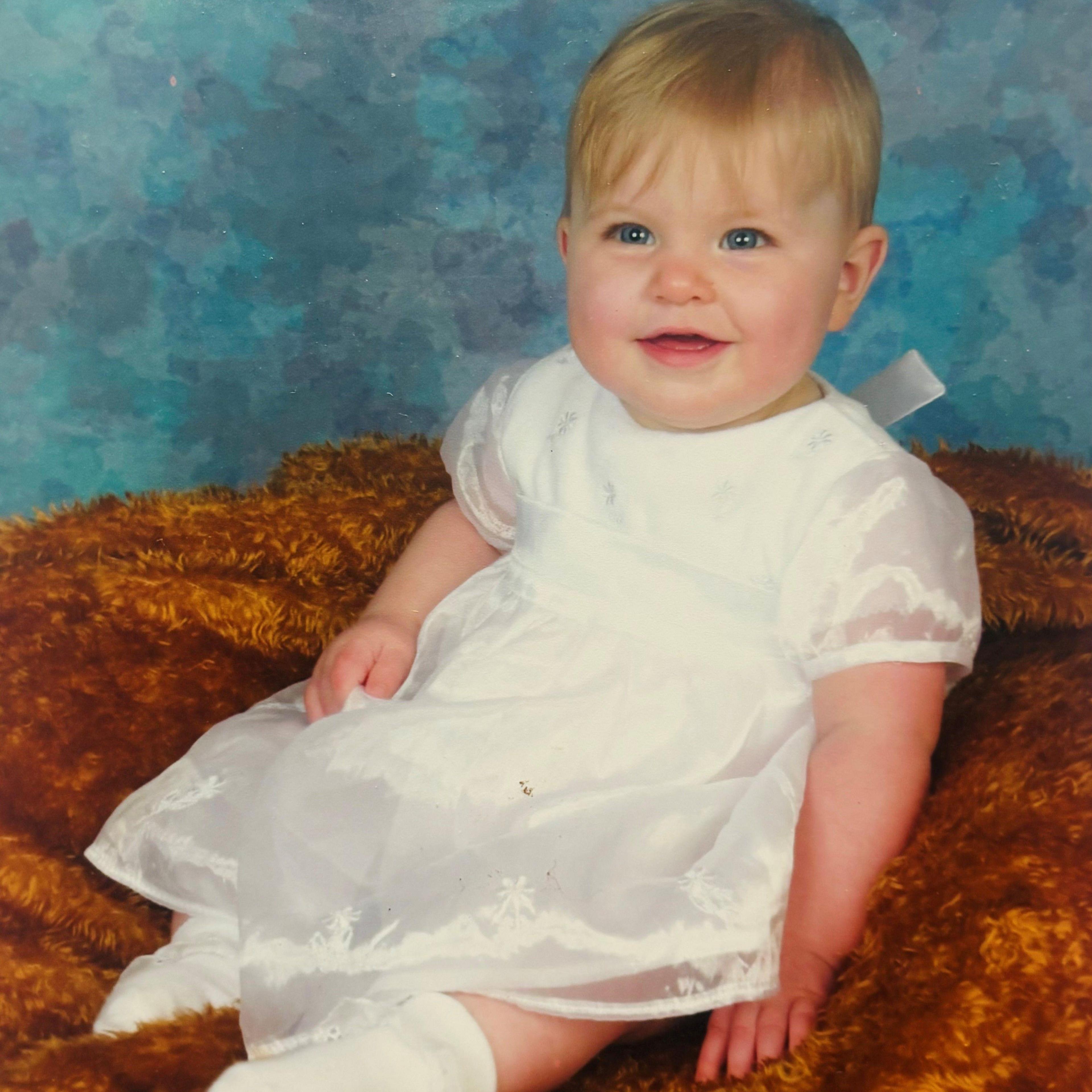 Midwife Leah Hobson pictured as a baby, smiling at camera, in a white dress.