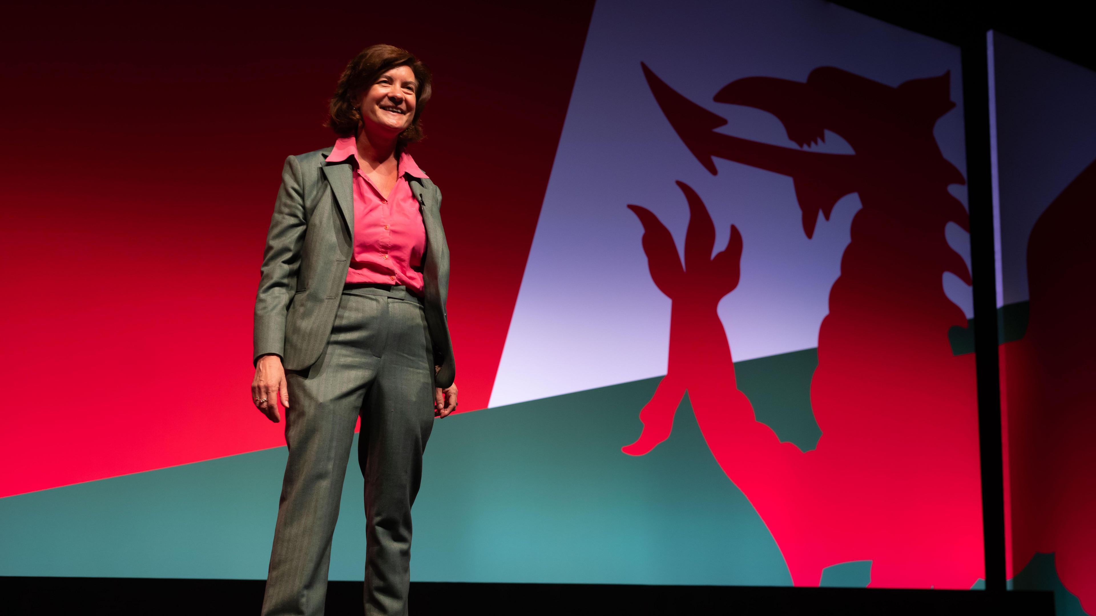 Eluned Morgan stands in front of an image of a Welsh flag