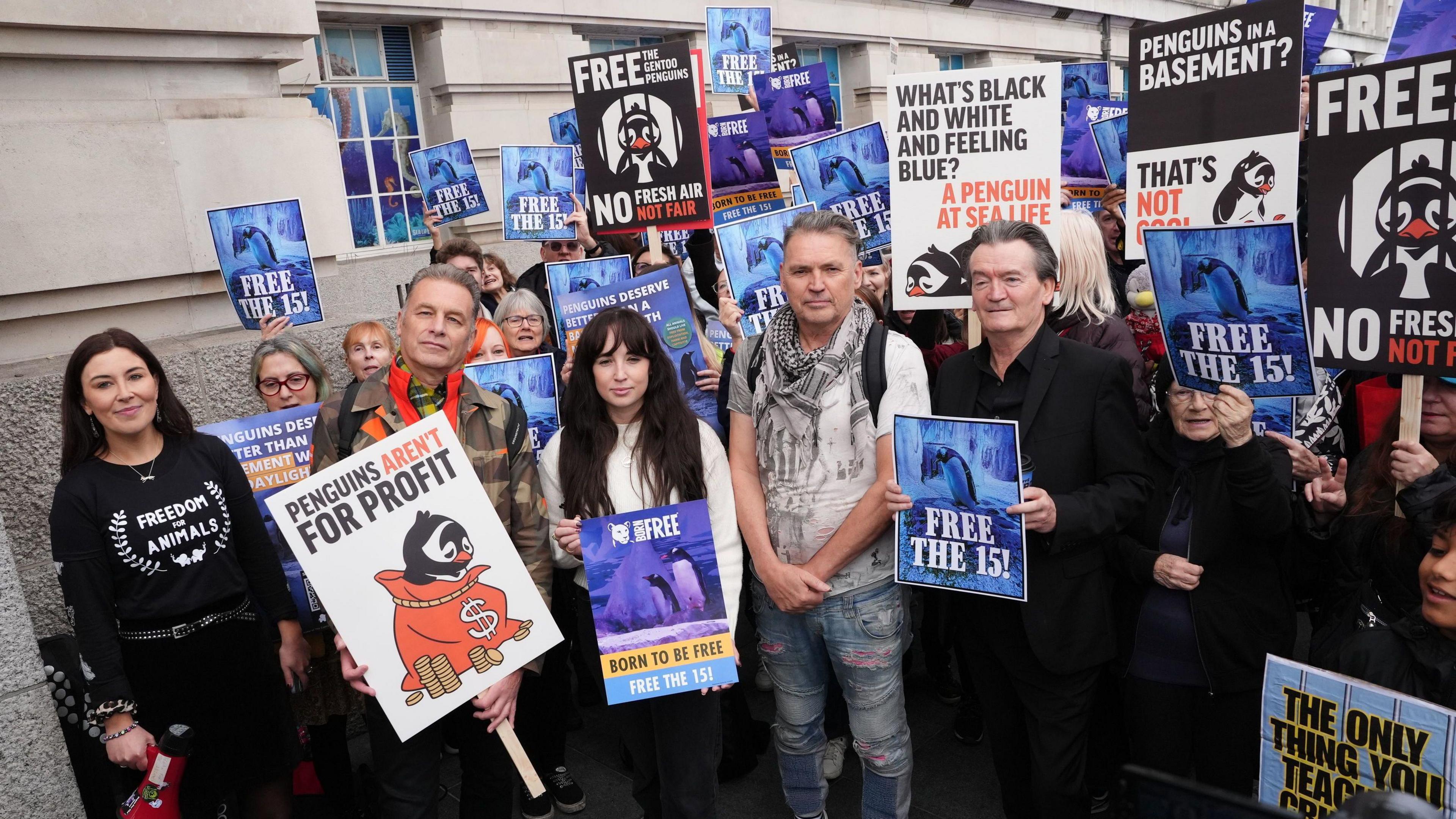 A group of campaigners holding signs campaigning for the release of penguins at an enclosure at Sea Life