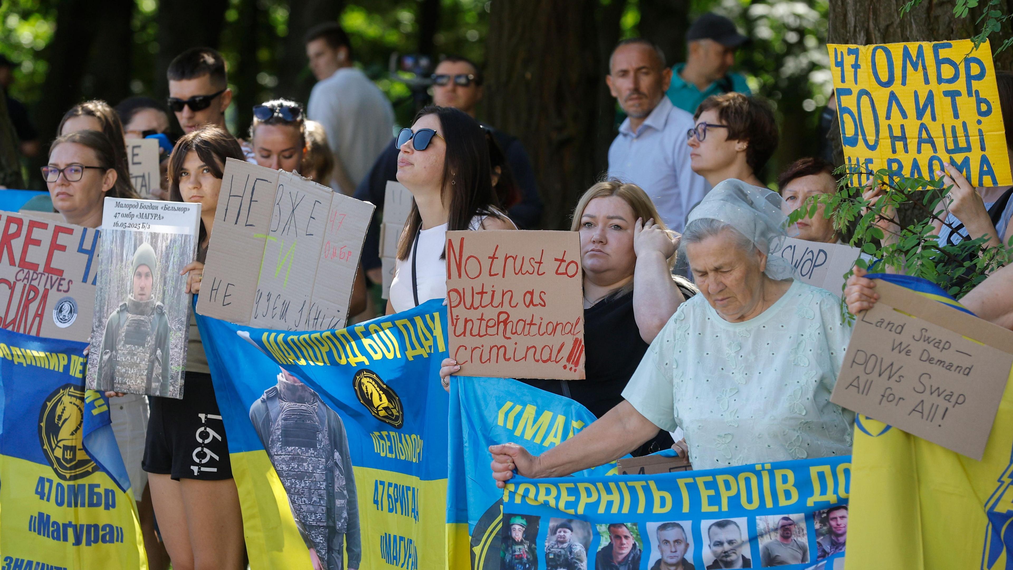 Ukrainians, including families of prisoners of war (POWs) and missing persons, participate in a rally called 'No land swap! We demand POW swap all-for-all' in front of the US embassy in Kyiv, Ukraine - a medium sized group of people are visible, all holding up signs, some in English and some in Ukrainian - one woman holds a sign saying 'No Trust to Putin as International Criminal!' - many of the protesters are holding up Ukrainian flags 
