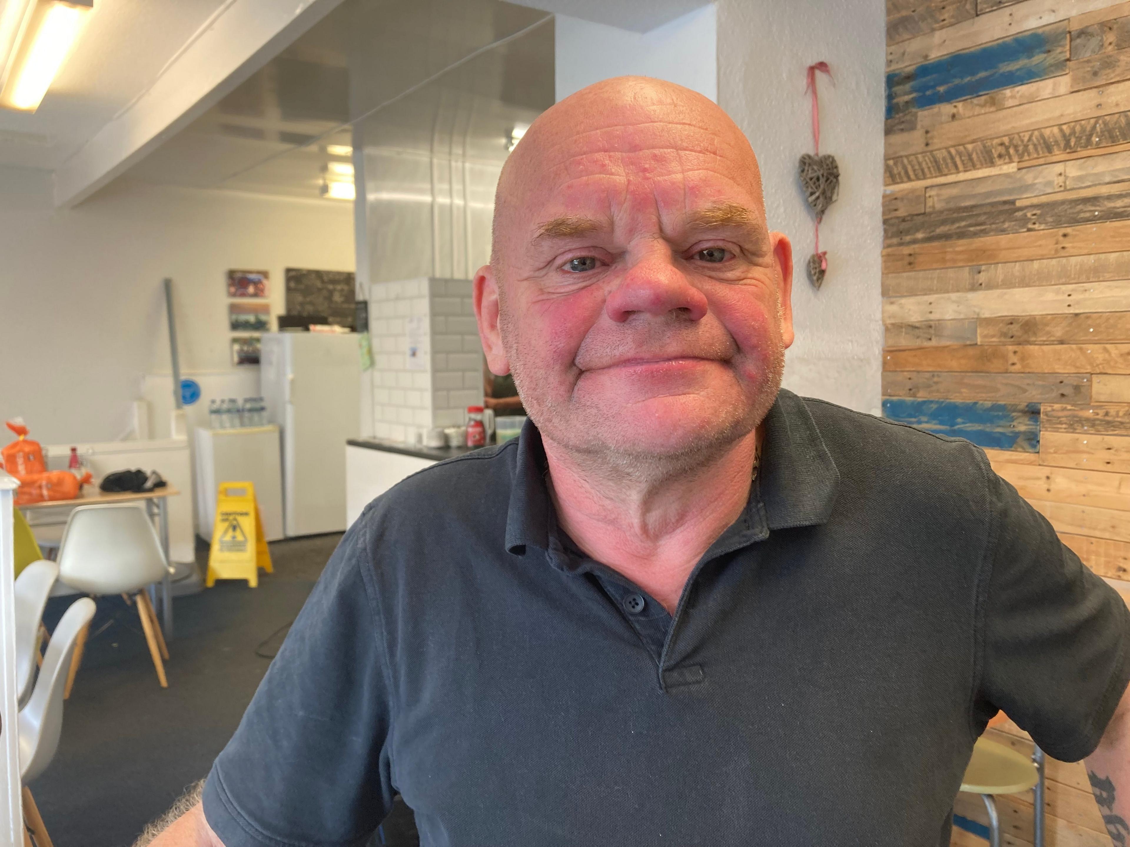 Cafe owner Mike Lambert wearing a blue polo shirt stands in the foreground with his cafe behind him