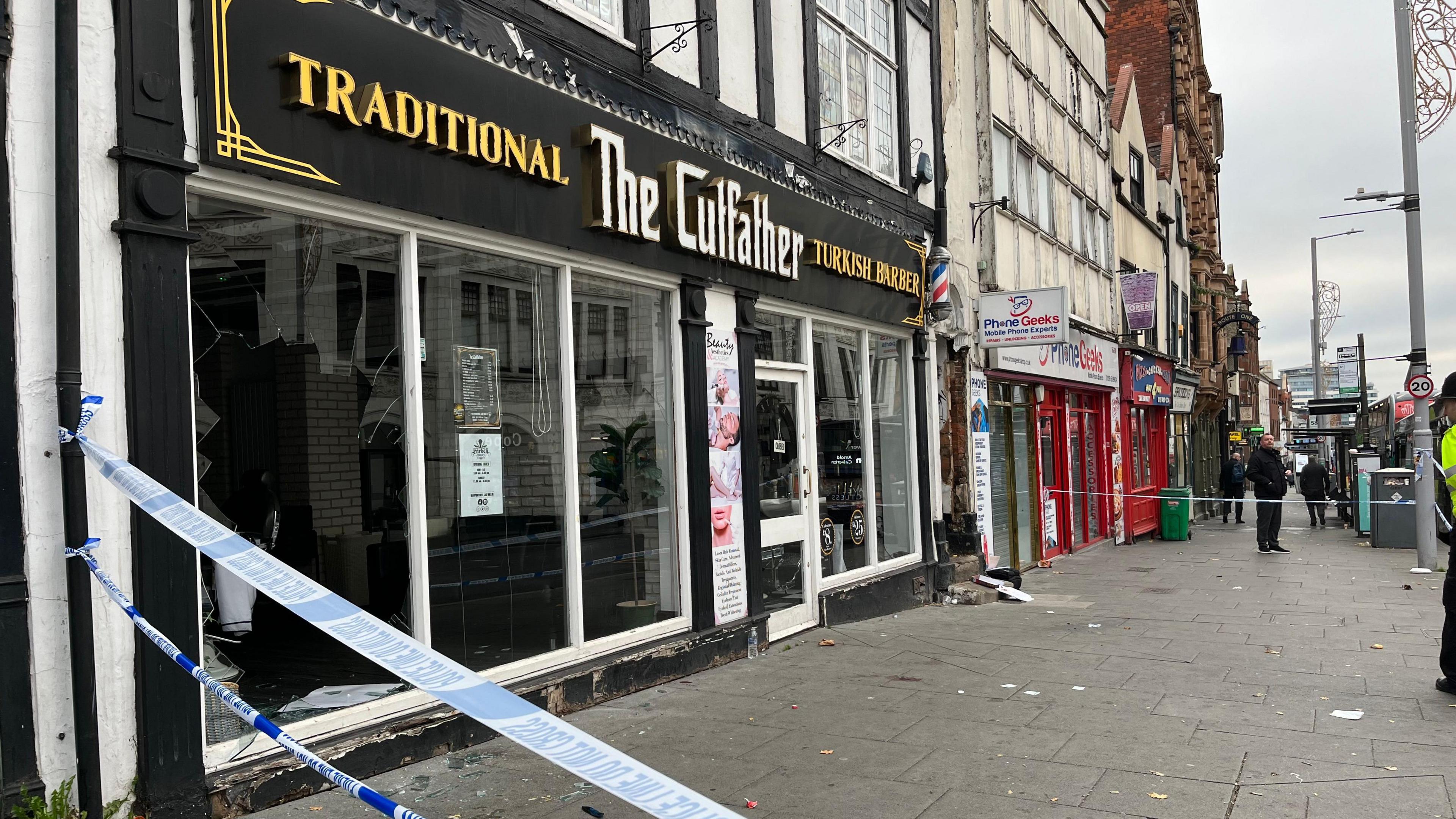 A police cordon around The Cutfather barber shop in Nottingham with a smashed window 