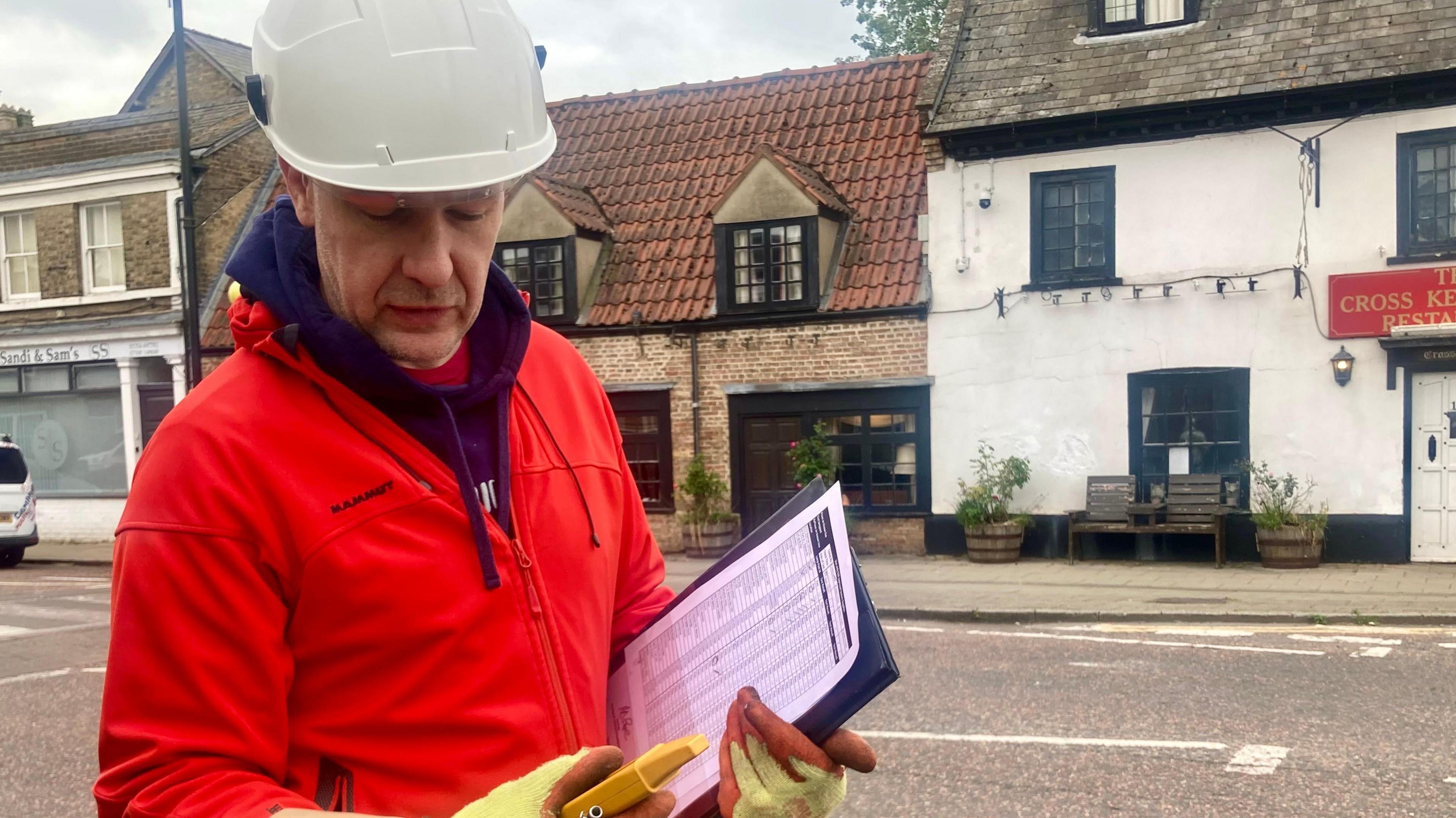 Richard Leney is wearing a safety hat and gloves and holding testing equipment. 