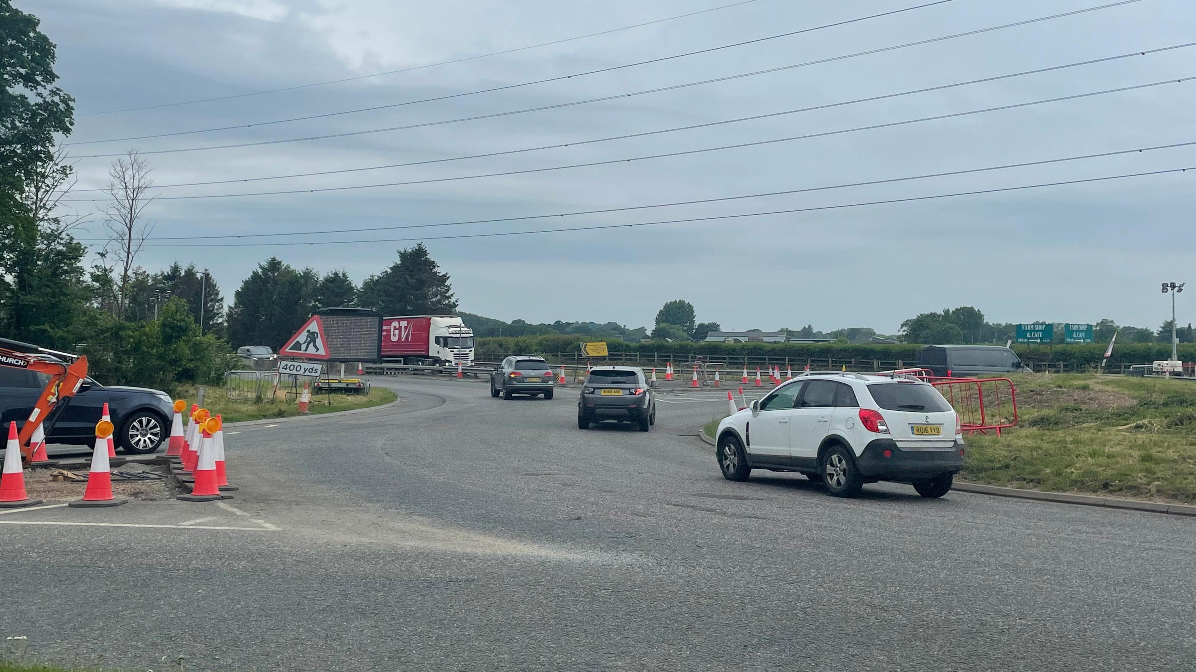 View of a large roundabout from the side with vehicles and a truck in the distance. Clear preparation for roadworks with lots of cones