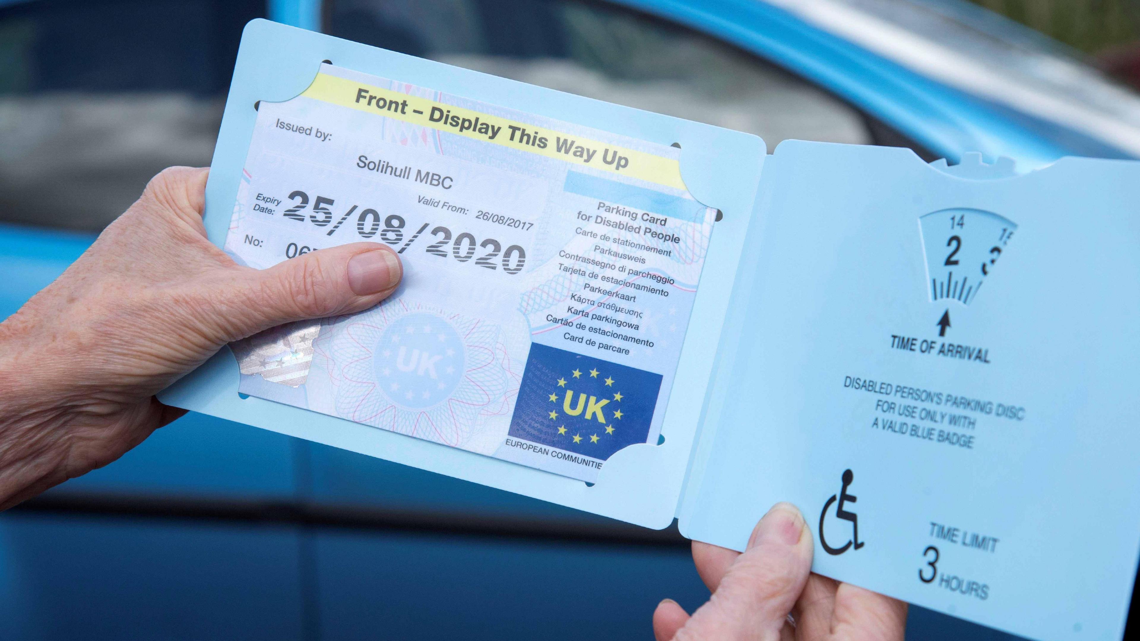 Woman's hands holding a Blue disabled driver, Badge parking