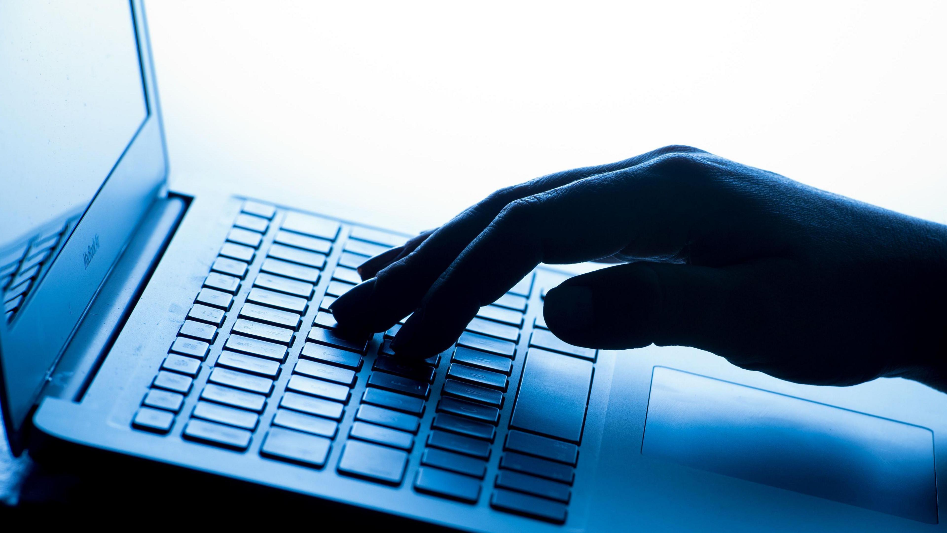 A hand on a keyboard in a blue shade of light.