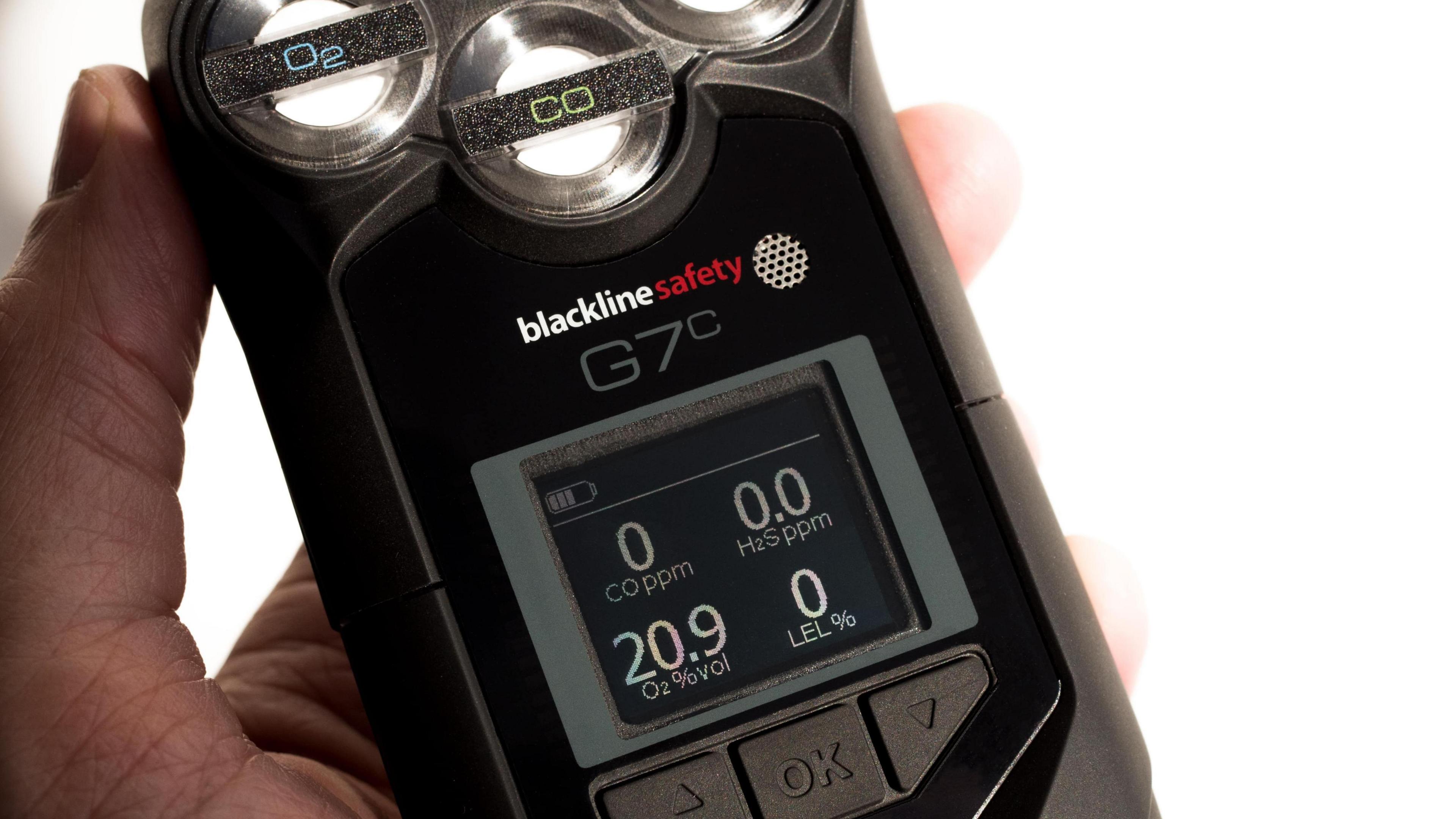 The picture shows a G7c gas monitor in the palm of a hand. It is black with an LED-type screen and has silver and black buttons on it. 