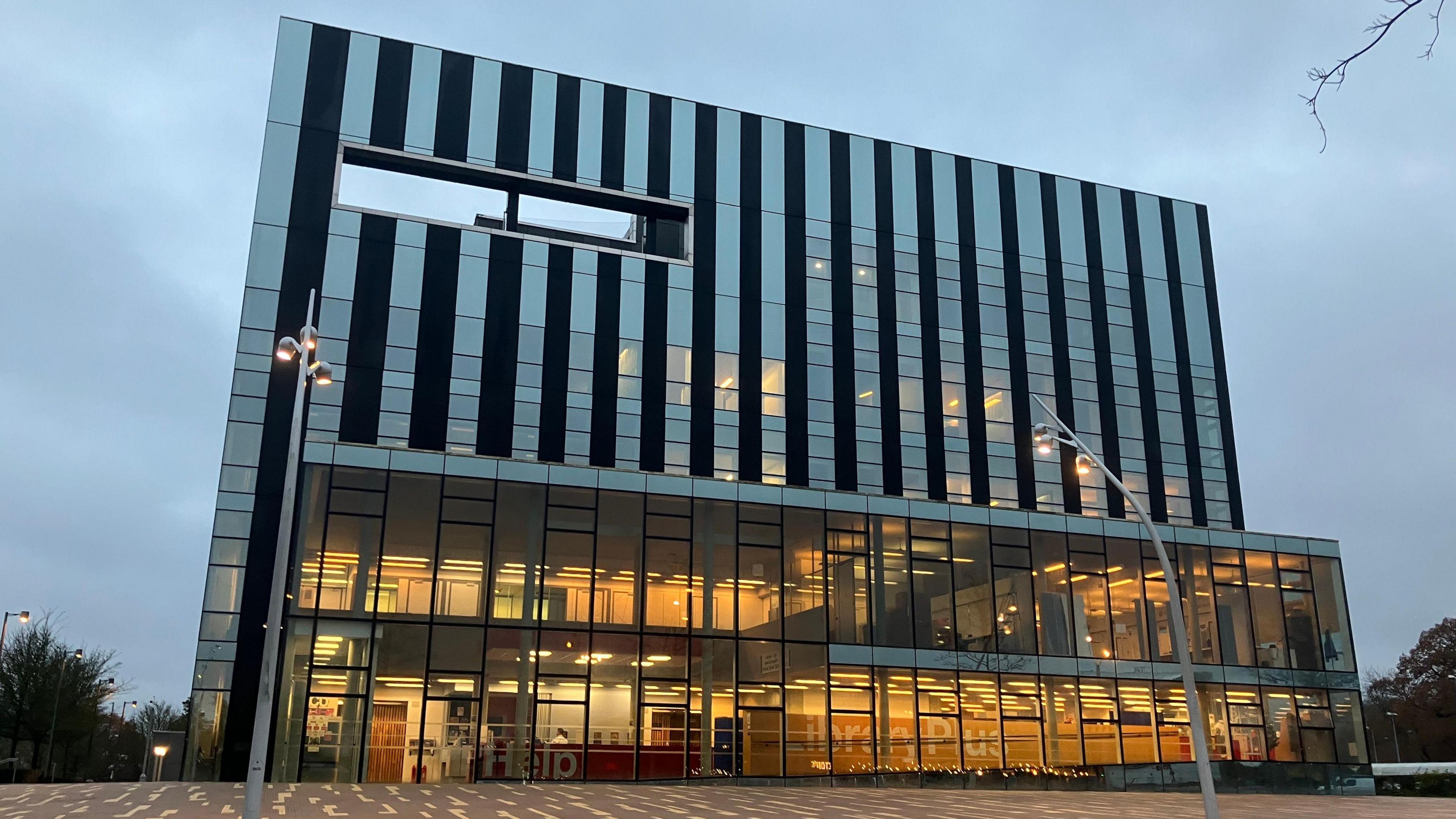 Corby Cube building, showing a large building, with lots of glass windows, with street lights outside the front. 