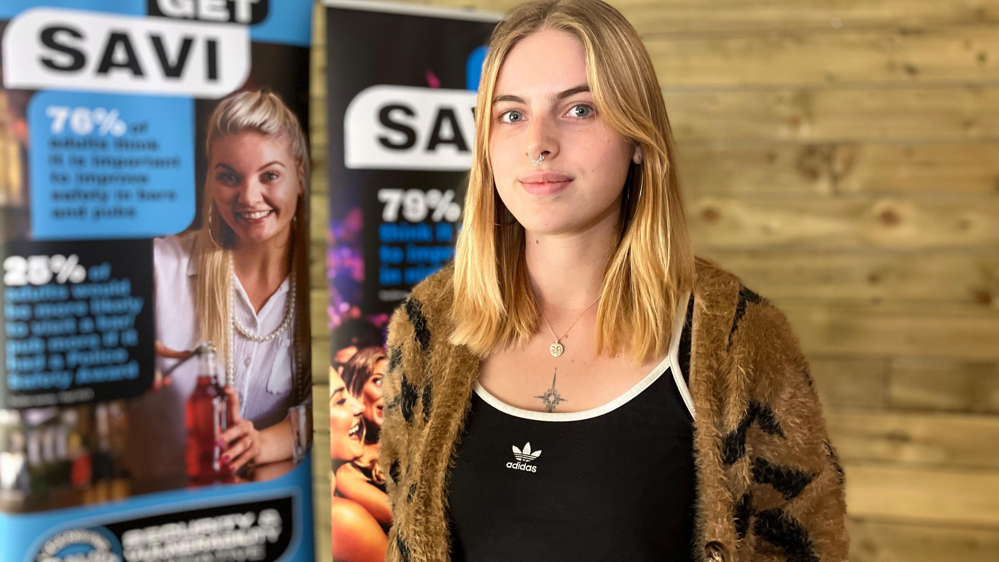 Antonia Cook with short blonde hair, wearing a black Adidas top and brown cardigan, smiling at the camera