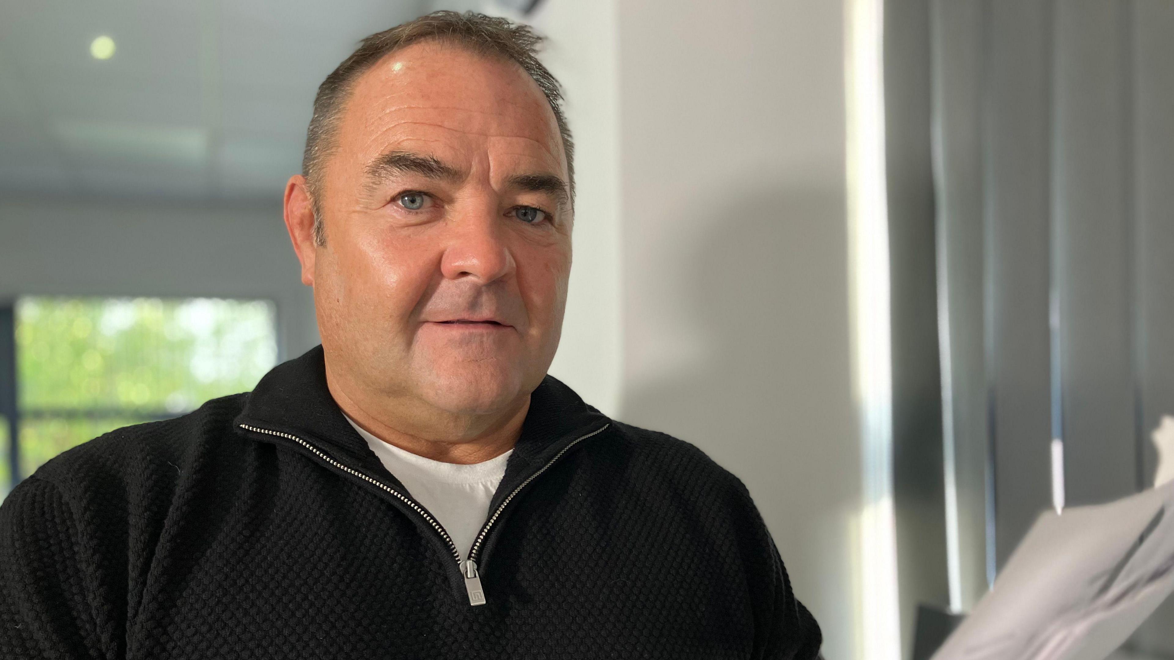 Craig Lakin is looking directly at the camera holding his phone contract in his left hand