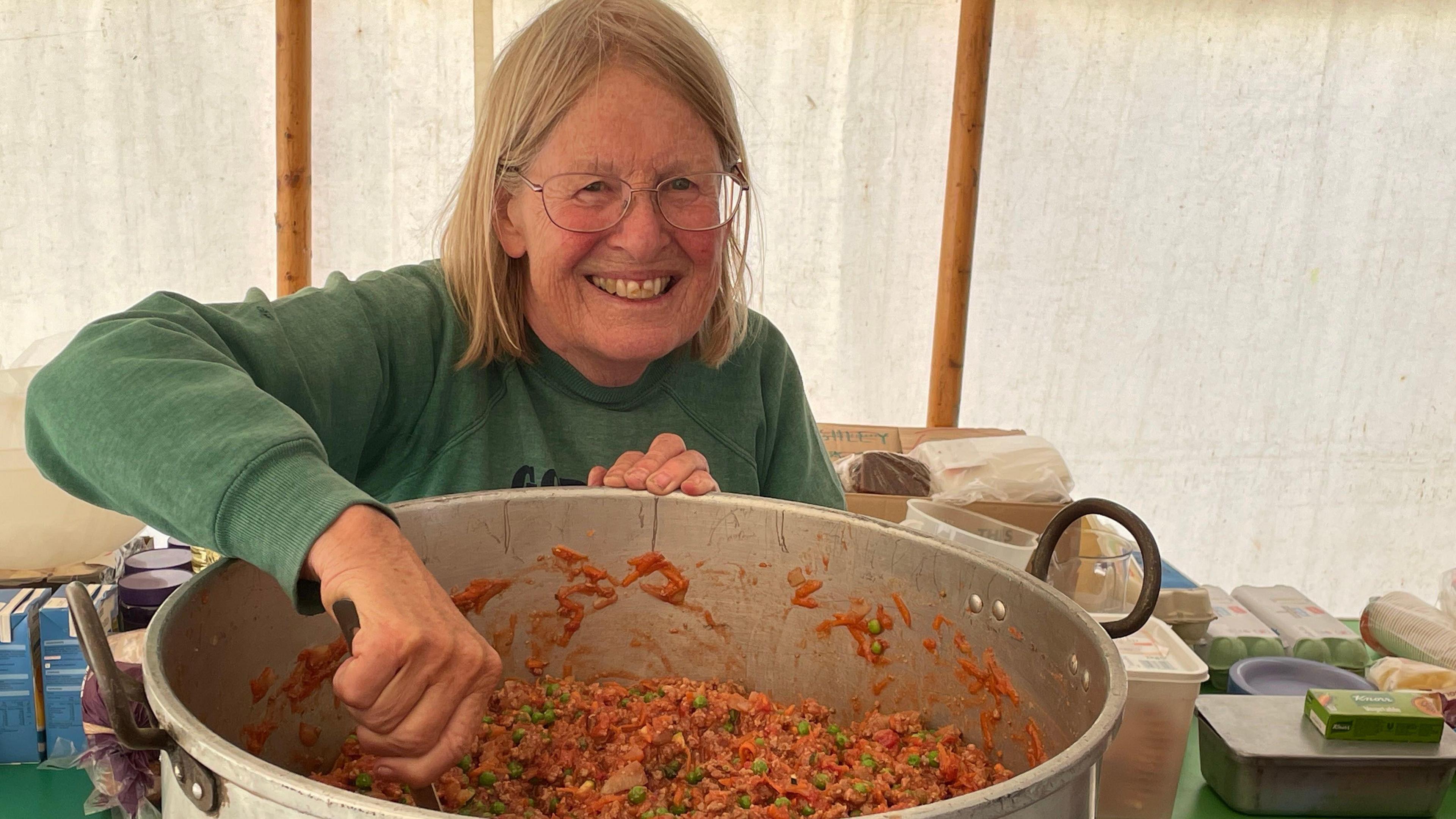 A woman is stirring a big pot with rice and peas in it. She is smiling at the camera.