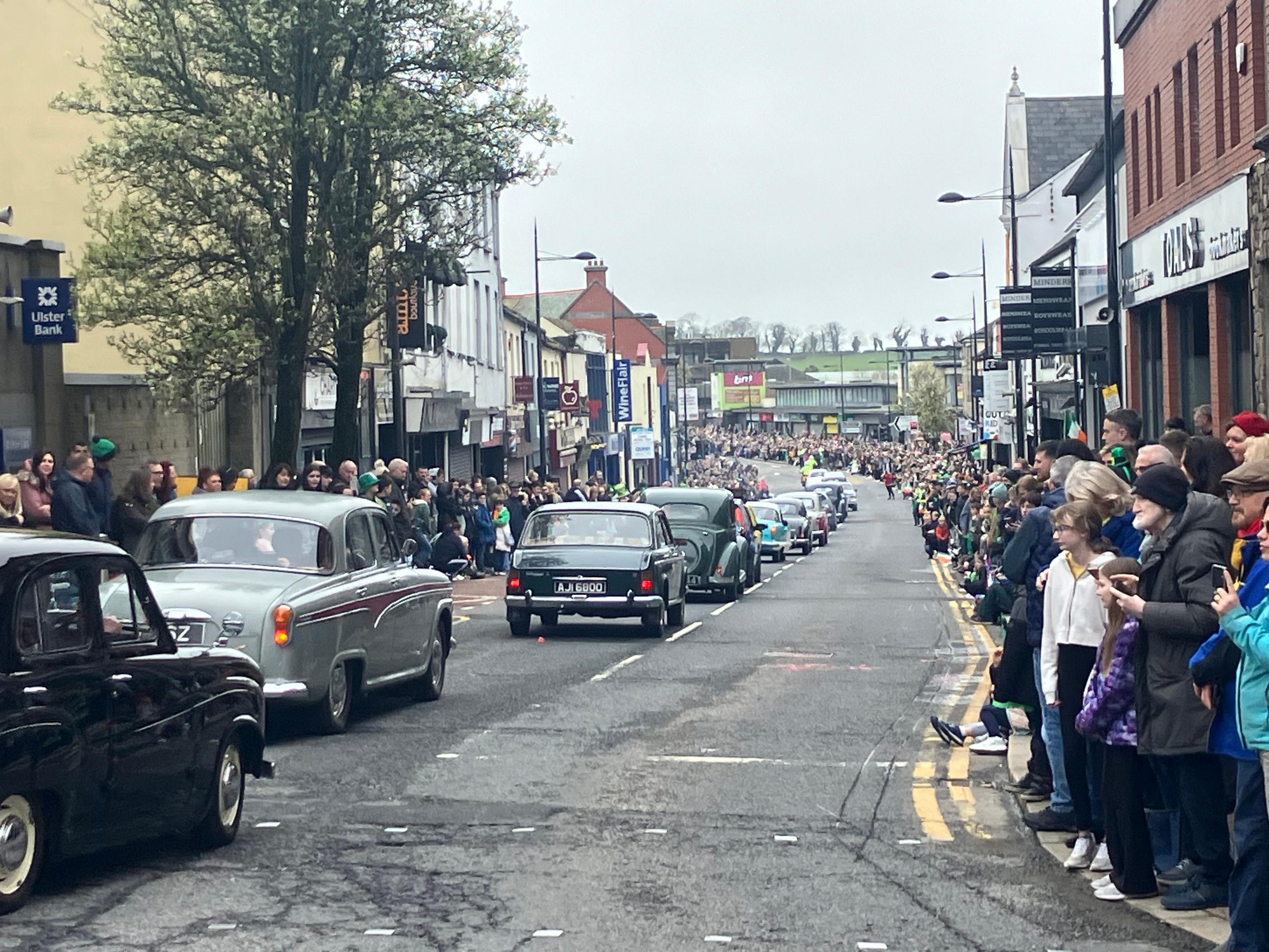 classic cars on a road with people watching