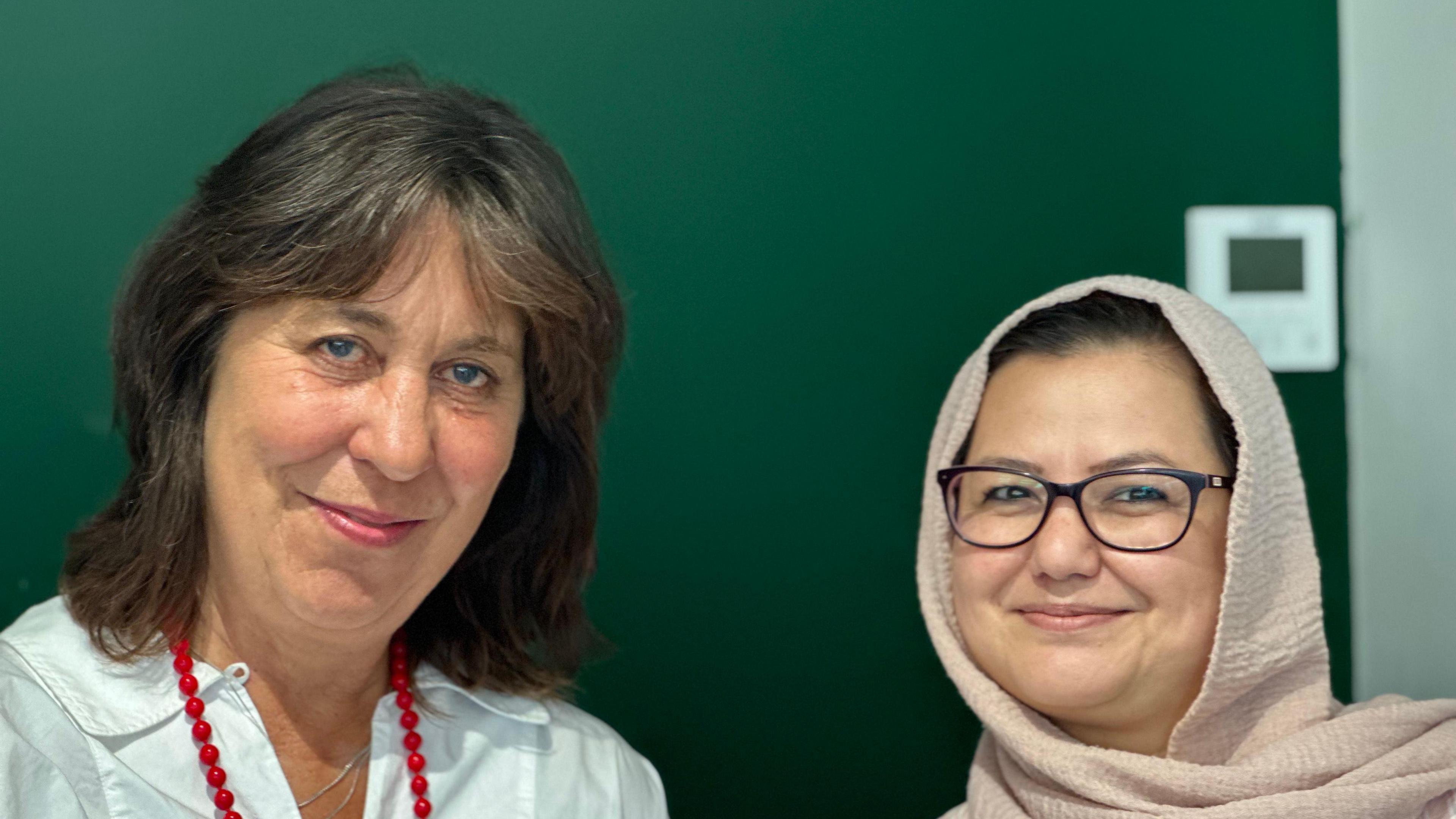 A smiling Sarah Cole (left) wearing a white shirt and red beads and a smiling Shakiba Alizadeh (right) wearing a nude headscarf and black rimmed glasses