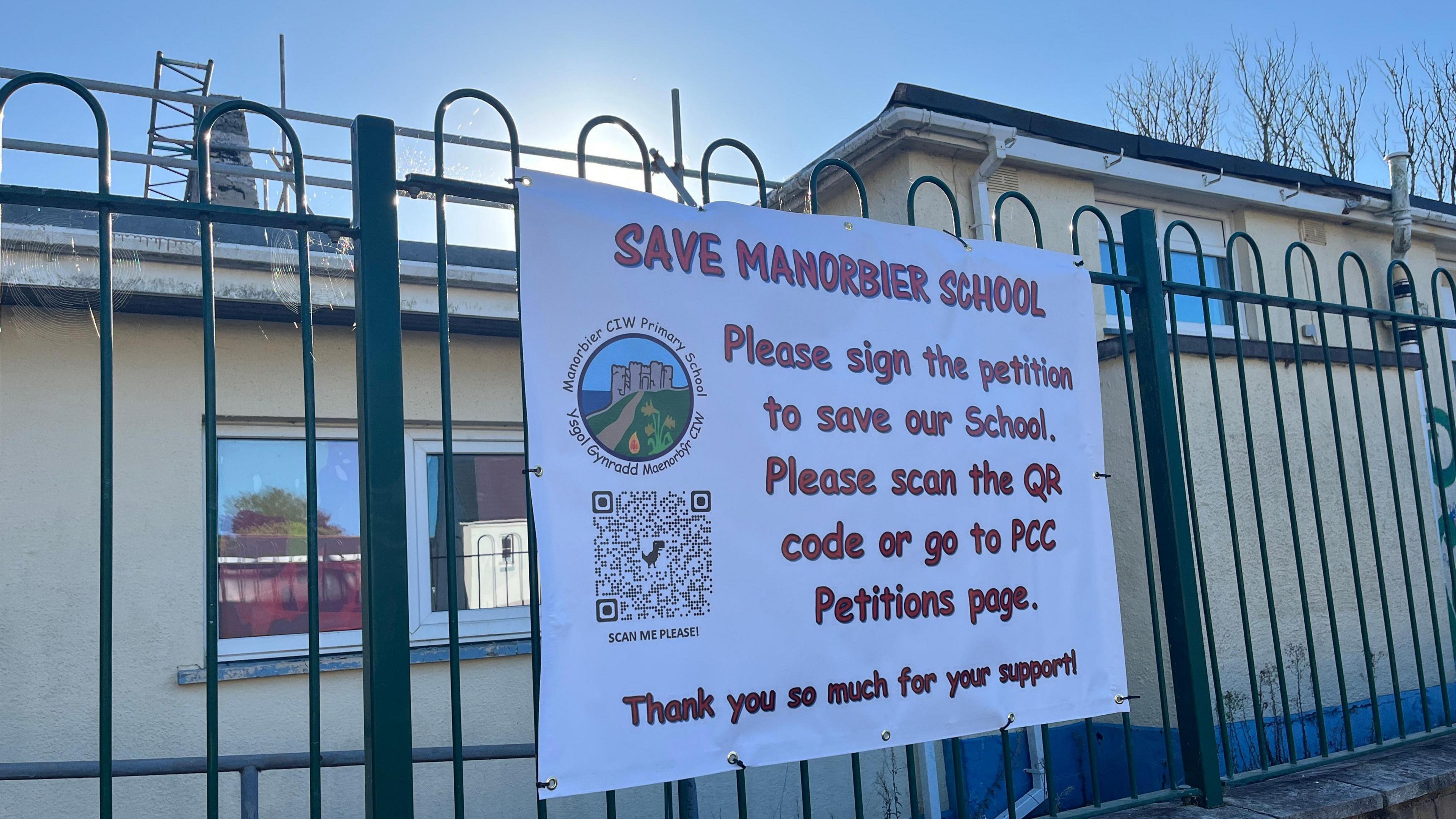 Exterior of Manorbier school with a printed banner asking people to sign the petition, with a QR code