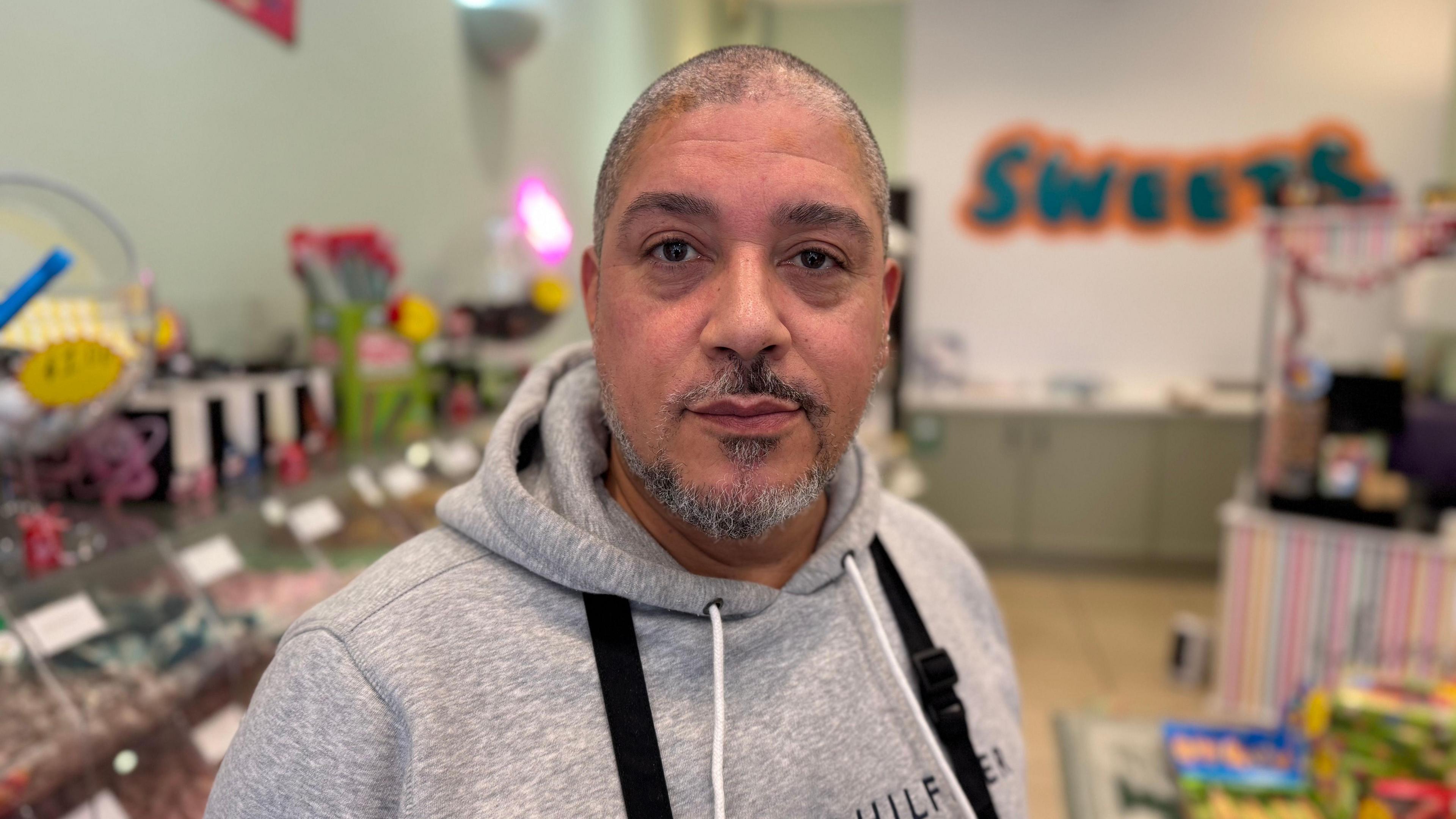 A man with shaven grey hair and grey facial hearing wearing a grey hoody while staring into the camera.