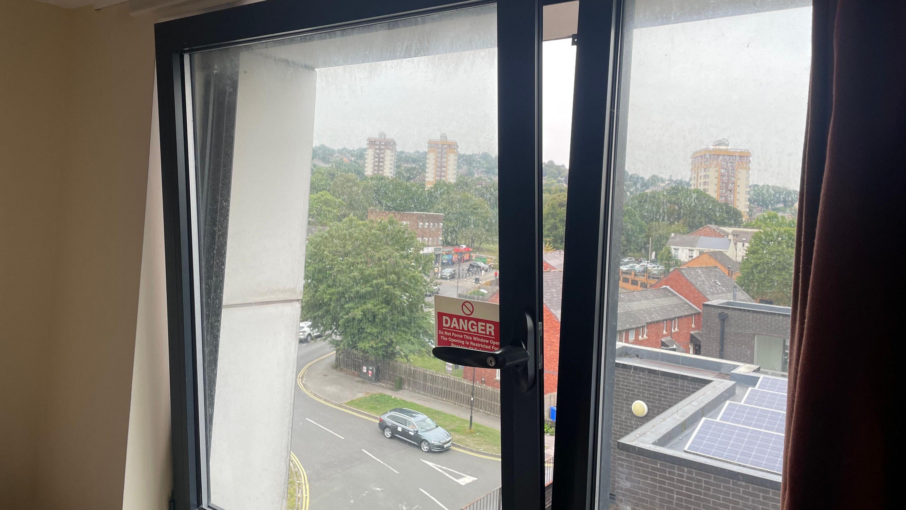 A hinge style window opened a few inches looking over a street several floors below