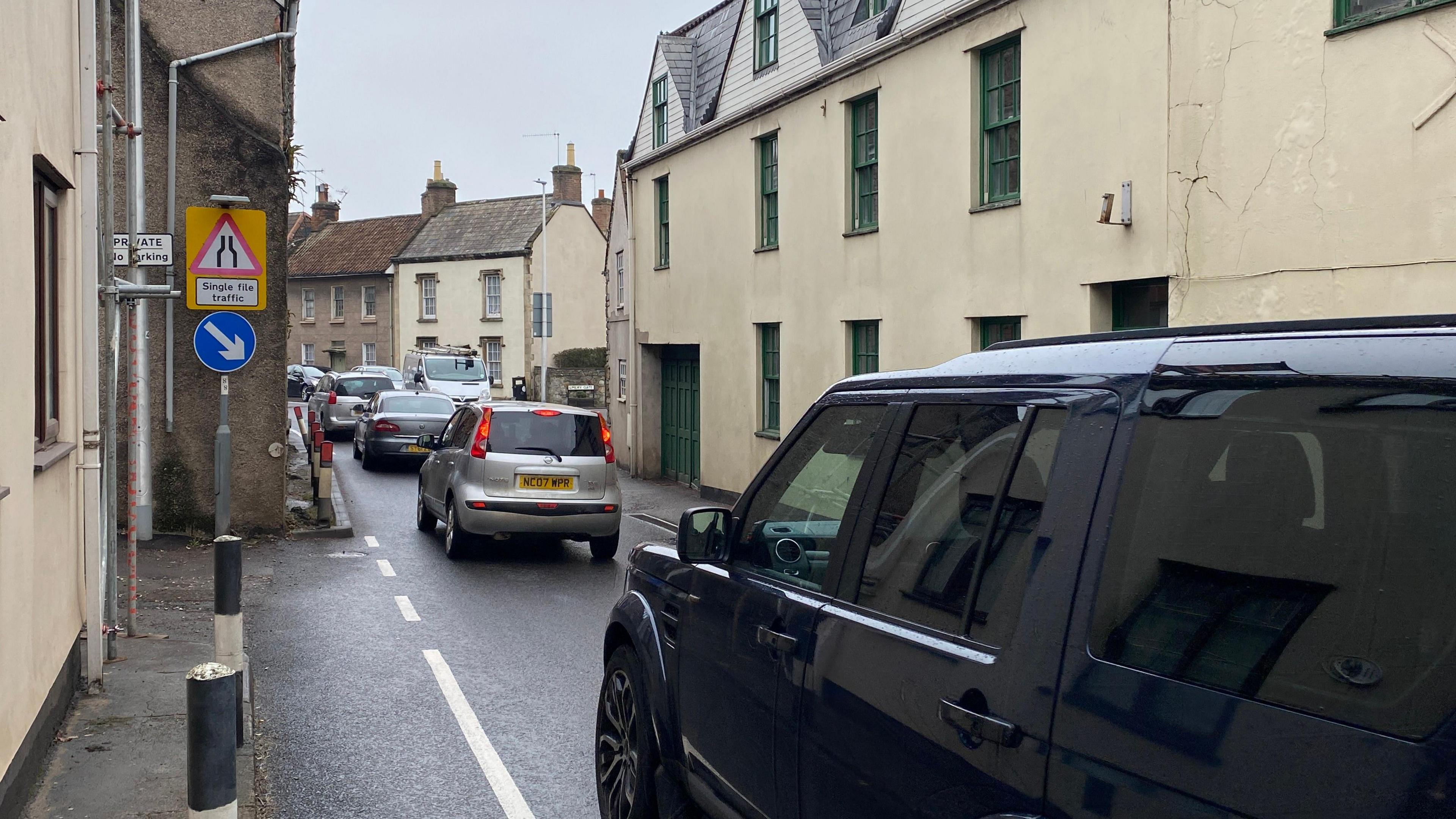 Cars driving through a narrow road in between houses