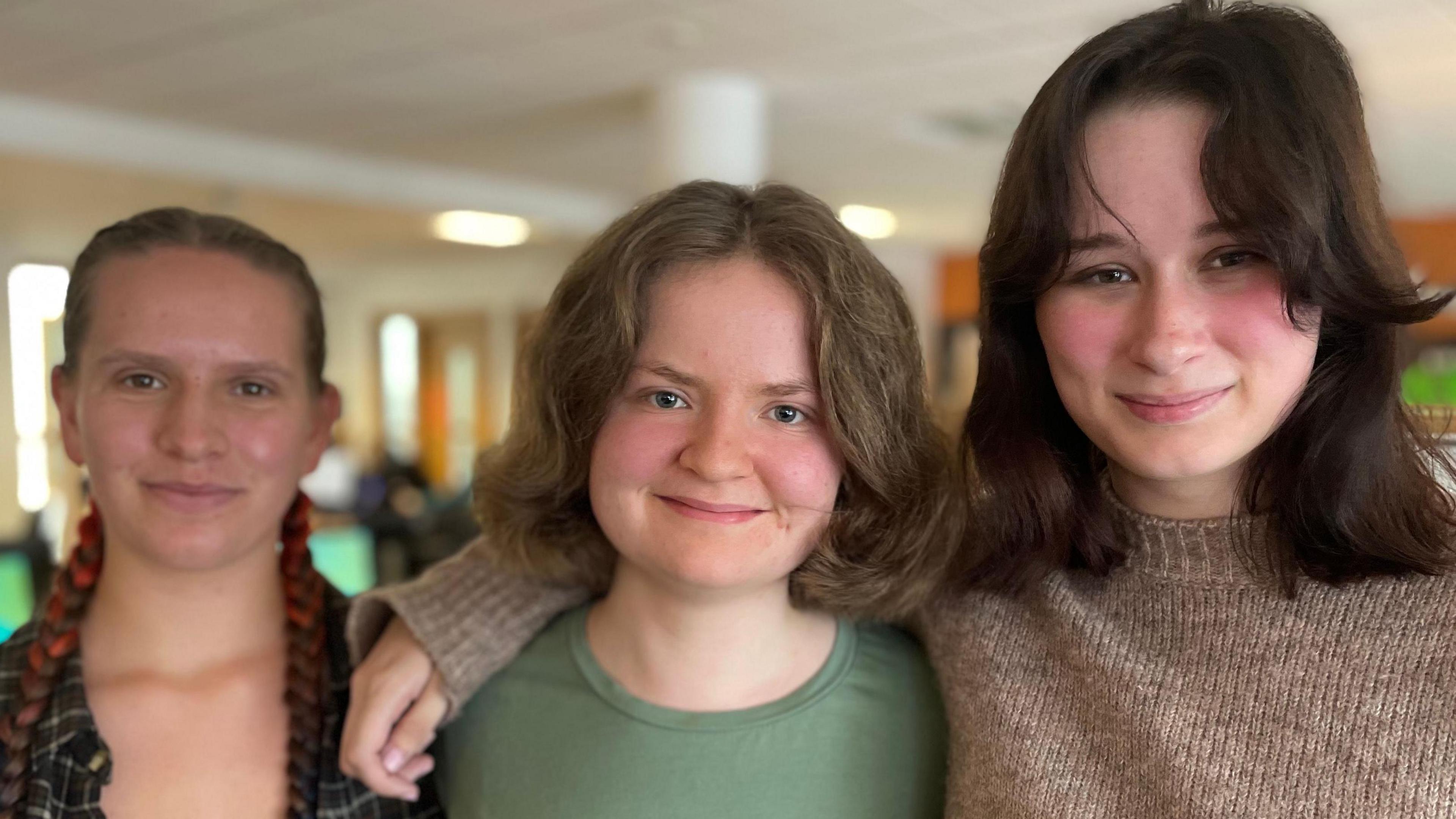 Coleg y Cymoedd students Olwen, Elinor and Maddie, aged 17 and 18, standing together in college library smiling at the camera